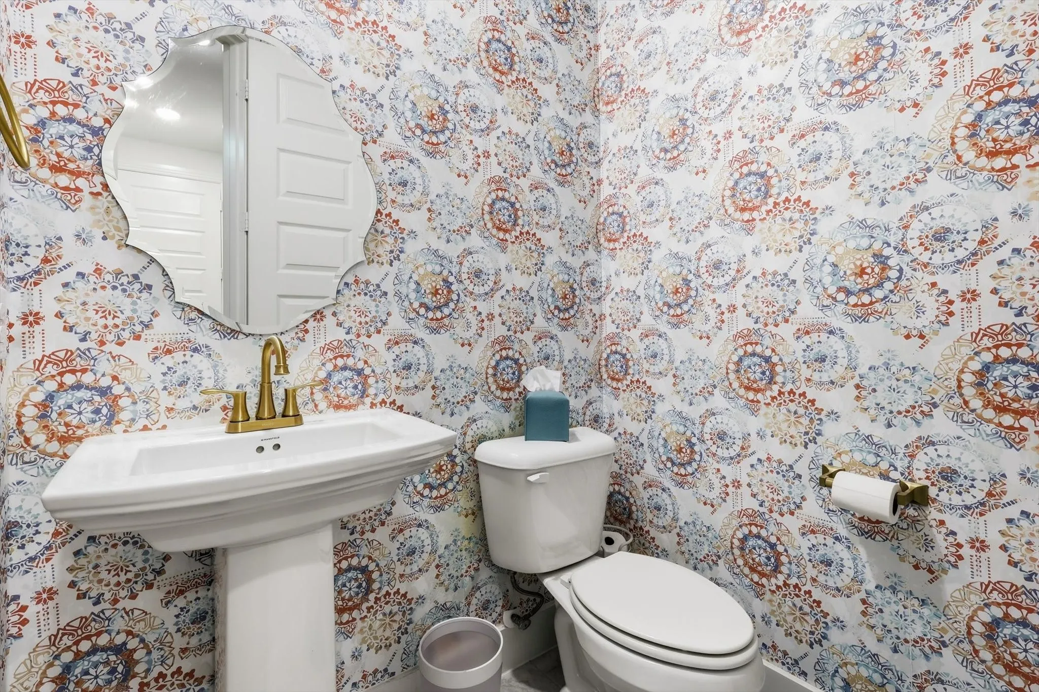 Pedestal sink with brass-finish faucet, framed by a decorative mirror