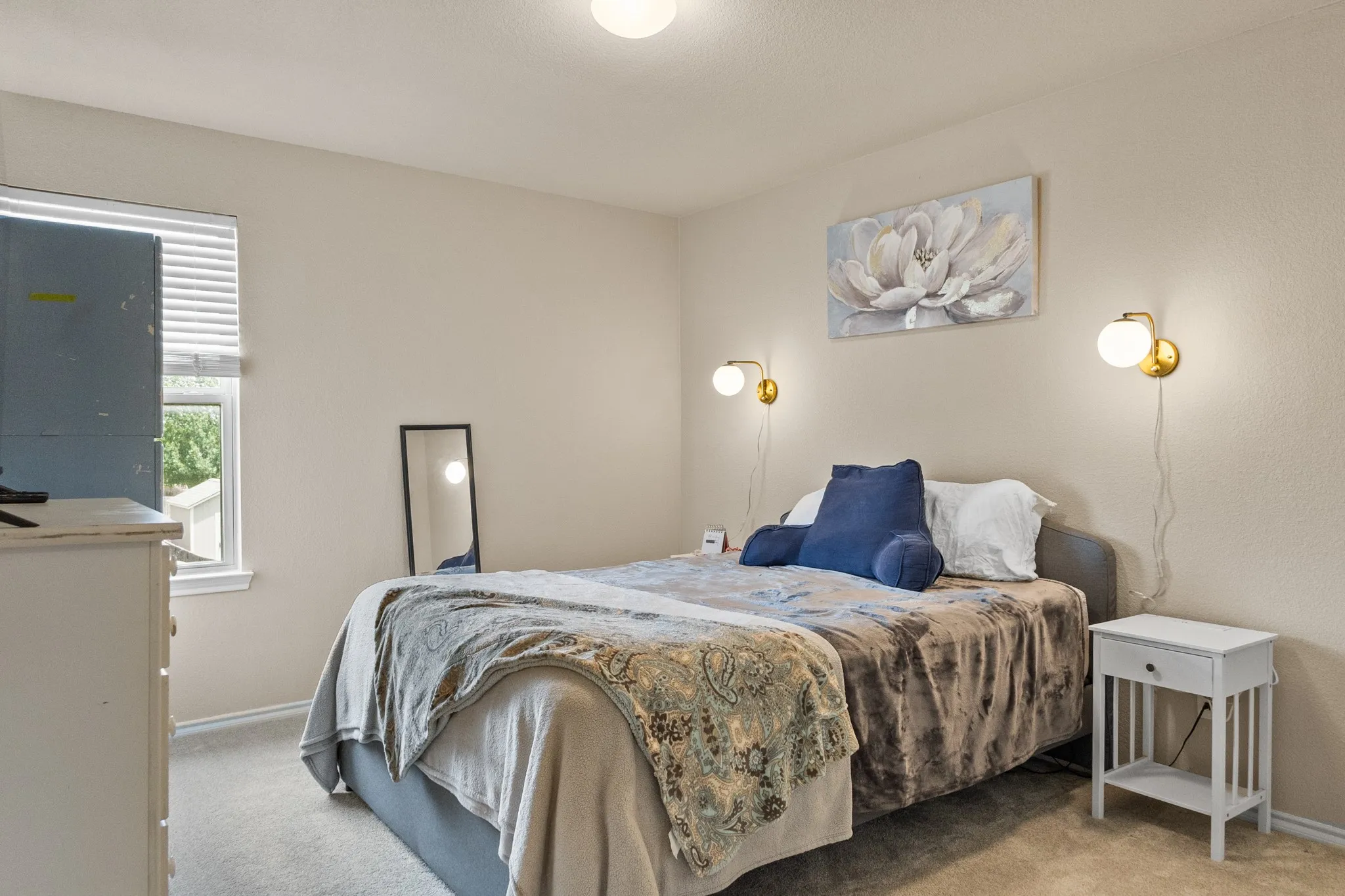 Carpeted room featuring a window with blinds, a built-in overhead light fixture, and two wall-mounted globe sconces