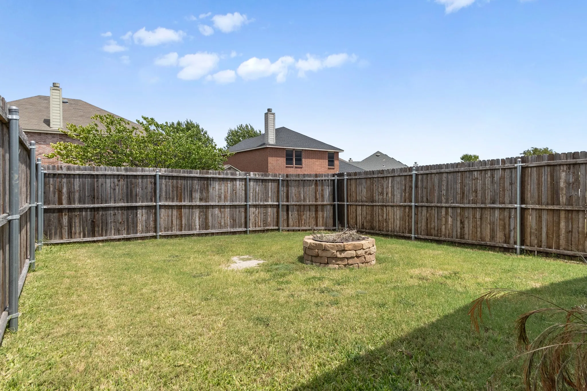 Expansive backyard featuring a stone-ringed fire pit, a perimeter wood privacy fence, and a natural grass lawn