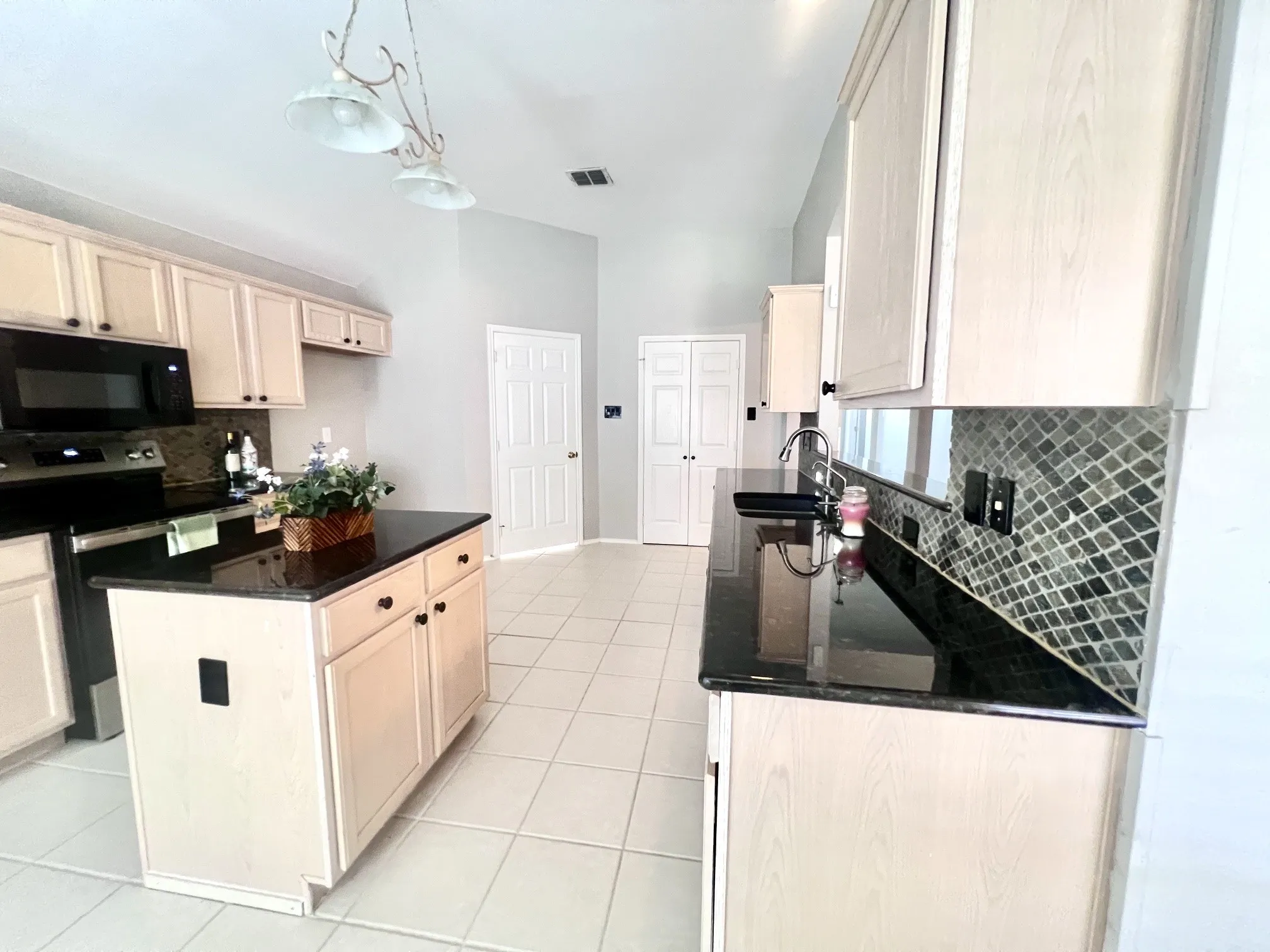 Kitchen featuring light wood-finish cabinetry, black countertops, a tile backsplash with diamond pattern, and tile flooring