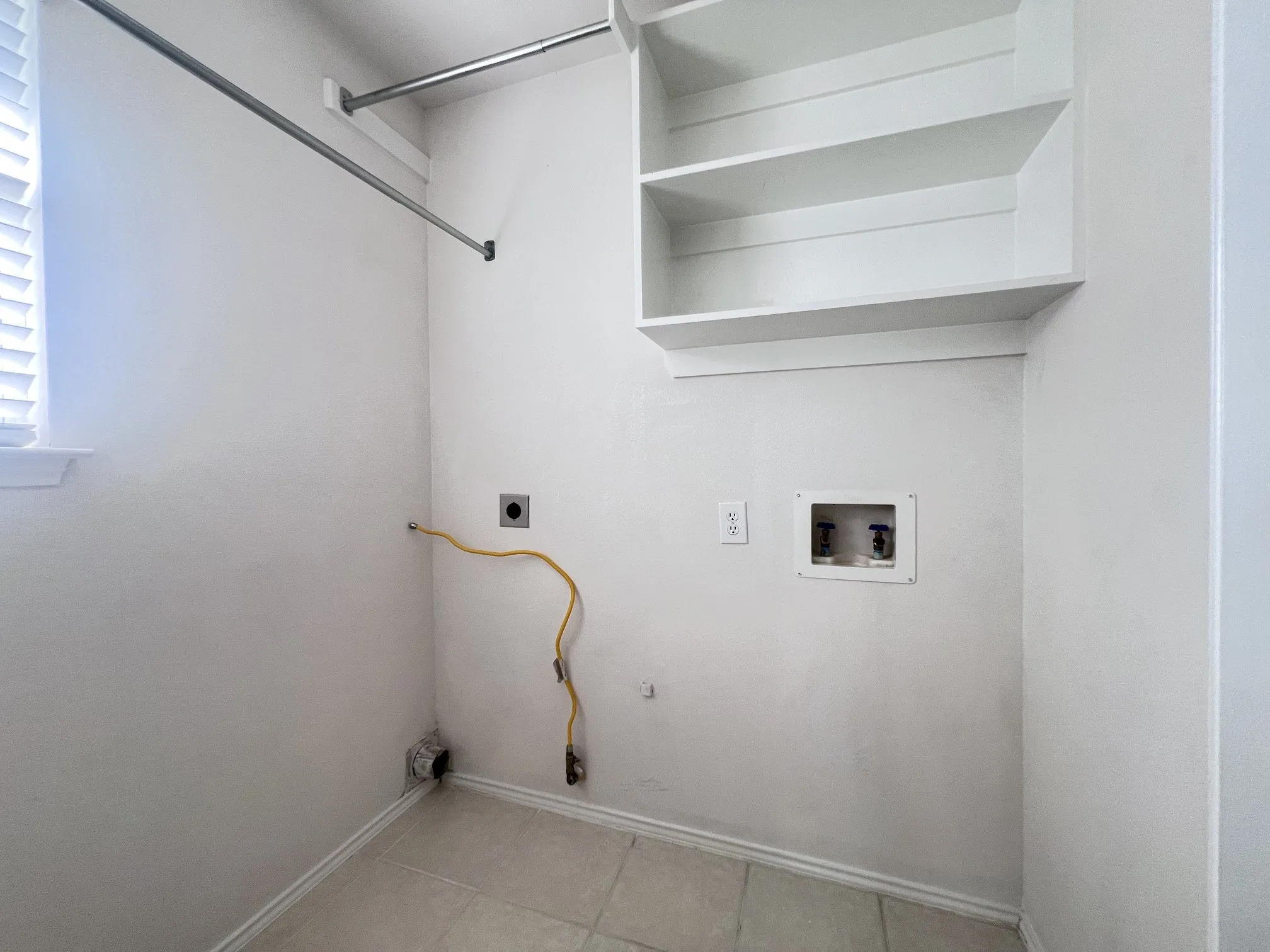 Laundry area featuring built-in shelving, a clothes hanging rod, and tile flooring