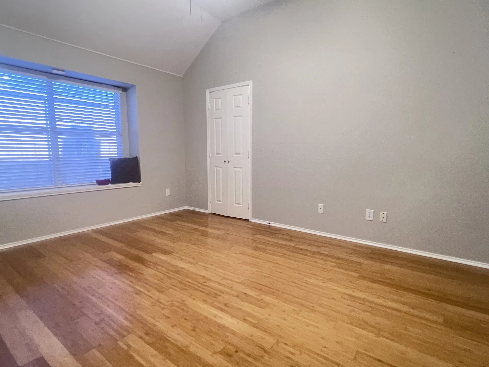 Vaulted ceiling room featuring light wood-finish flooring, a window with horizontal blinds, and a built-in window seat
