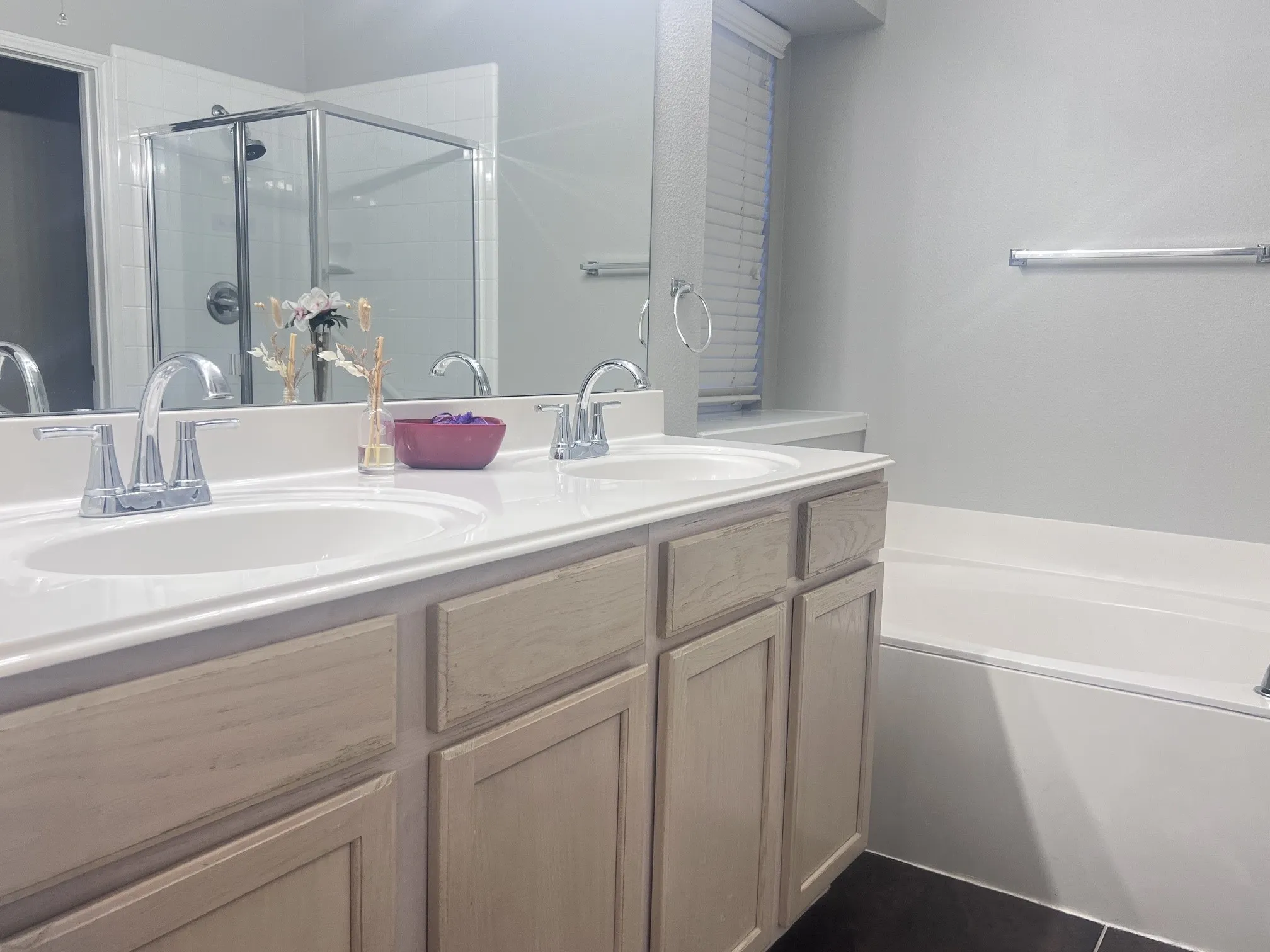 Dual sink vanity with light wood-finish cabinetry, chrome fixtures, and a white countertop