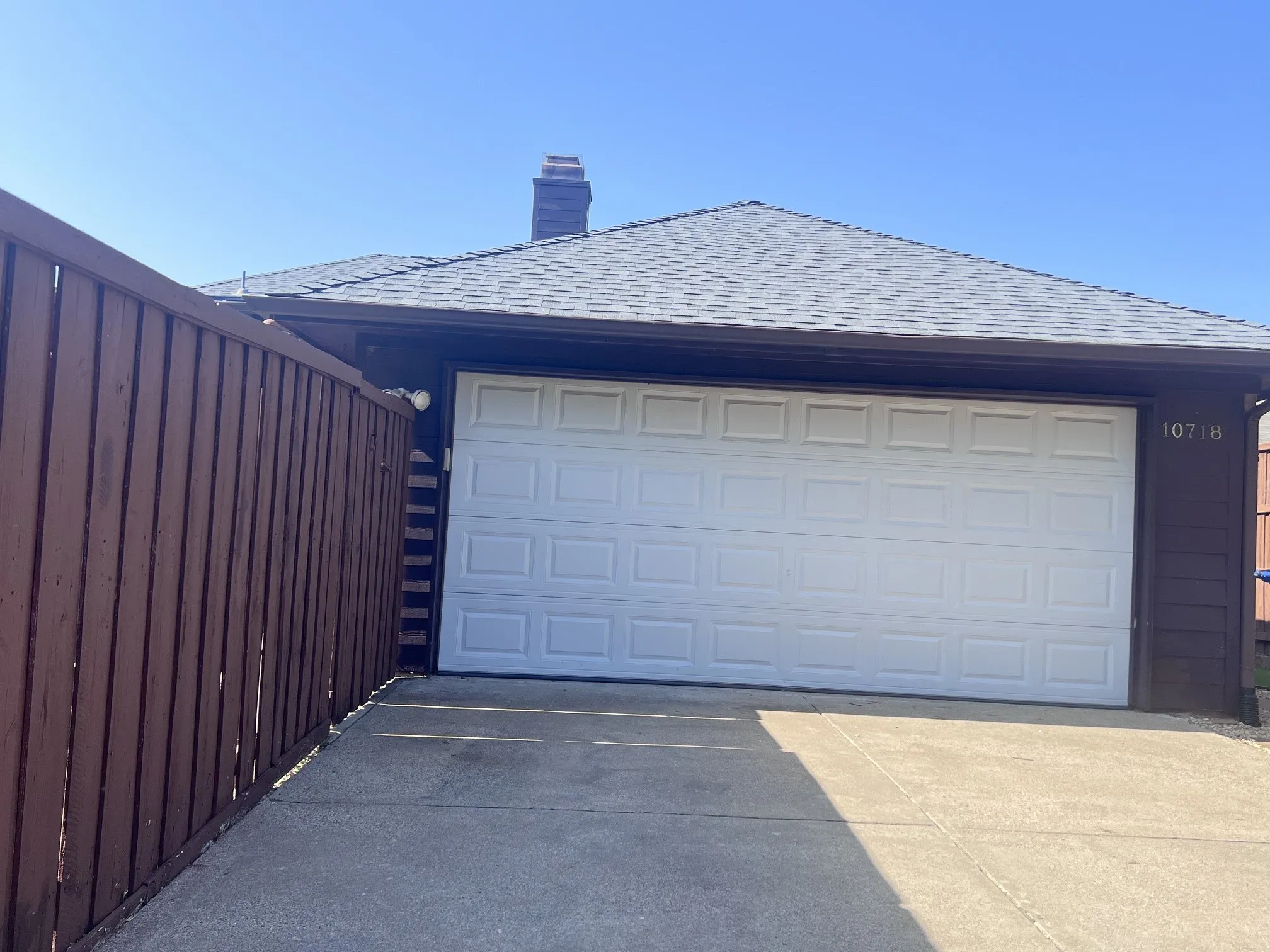 Attached garage featuring a white paneled door, gray shingle roof, and dark brown exterior siding