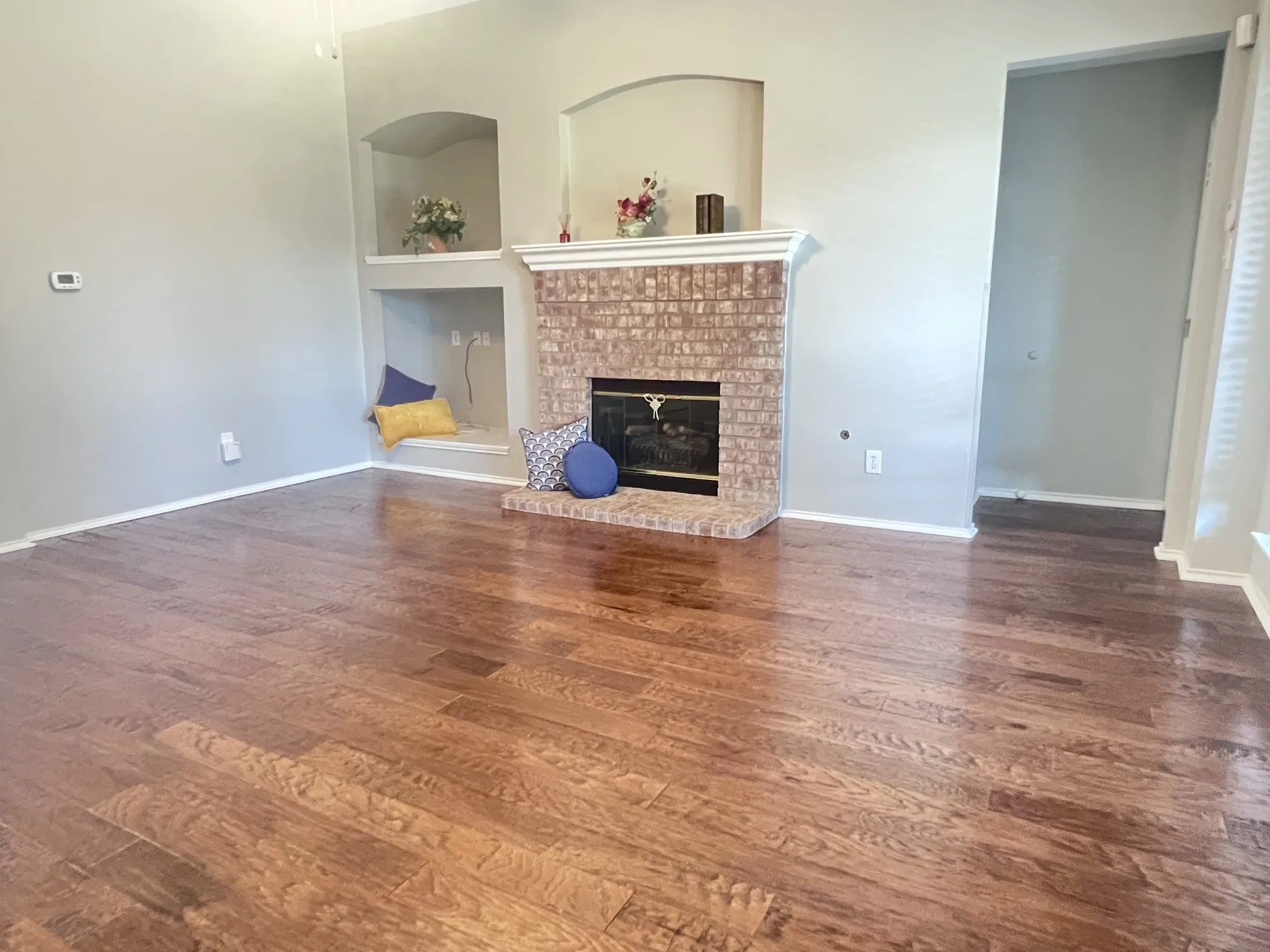 Spacious room featuring wood-finish flooring, a brick fireplace with mantel, and built-in arched display niches