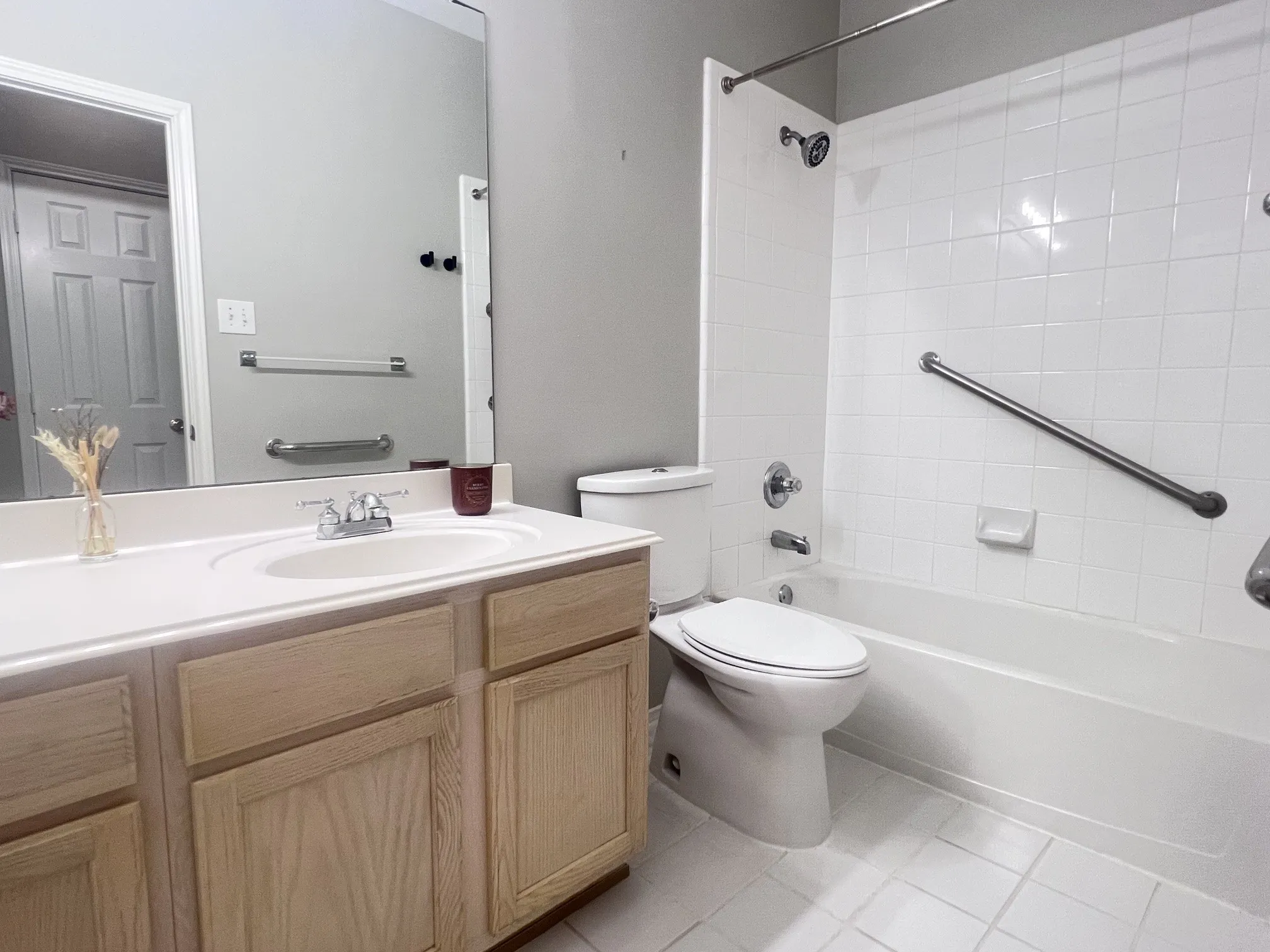 Bathroom featuring a light wood-finish vanity with a white countertop and integrated sink, a large wall-mounted mirror, a tub/shower combination with white tile surround, and a toilet