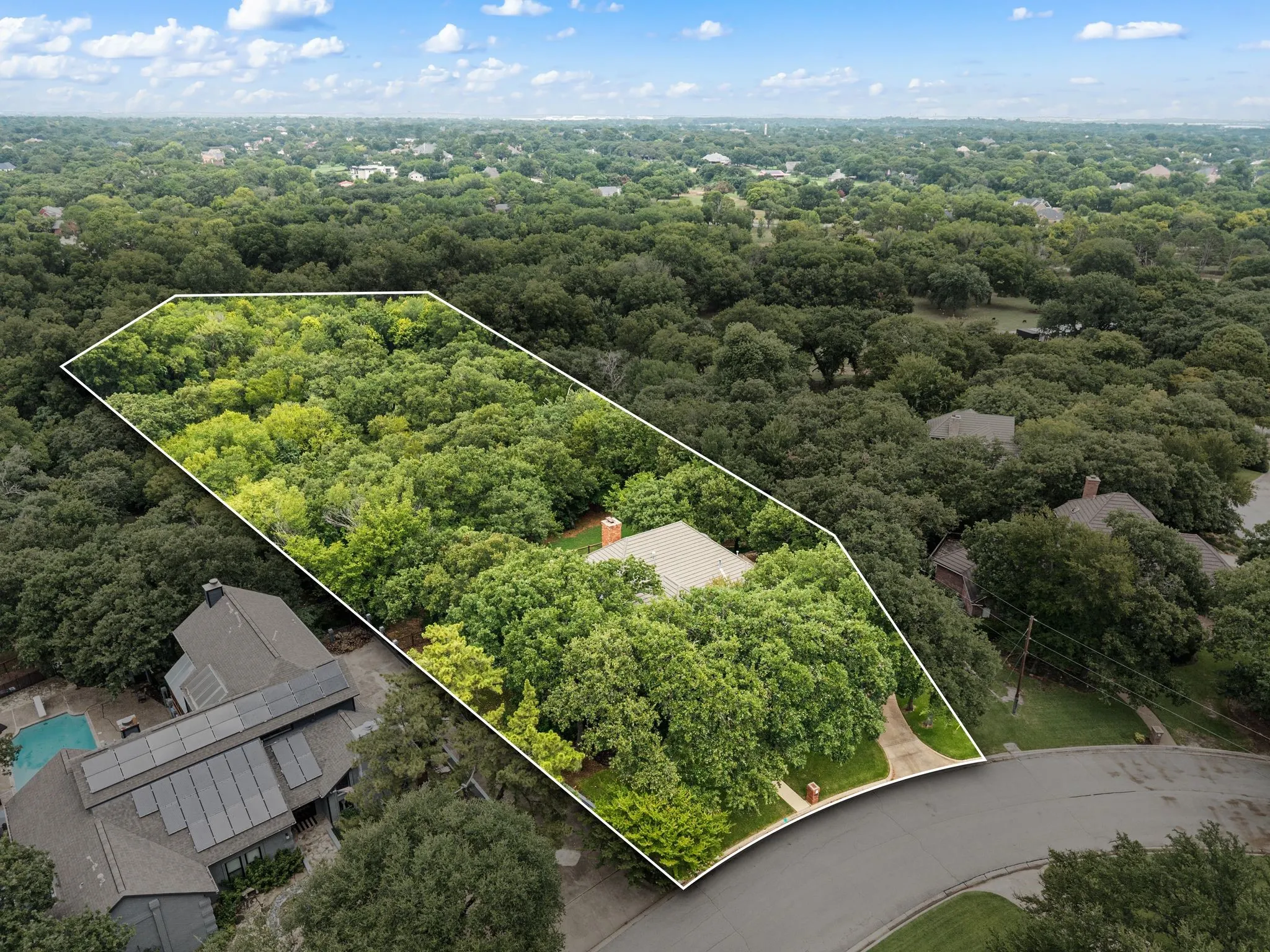 Aerial view of a wooded property outlined in white, featuring a single-story residence with a light-colored roof and a visible chimney