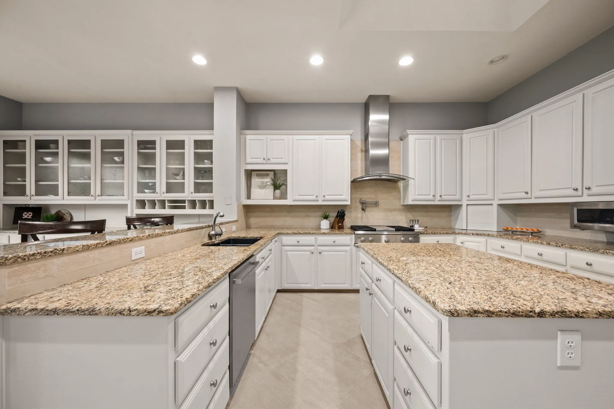 Kitchen featuring a large central island with a granite countertop, white cabinetry with display glass doors, stainless steel appliances, a tile backsplash, and recessed lighting