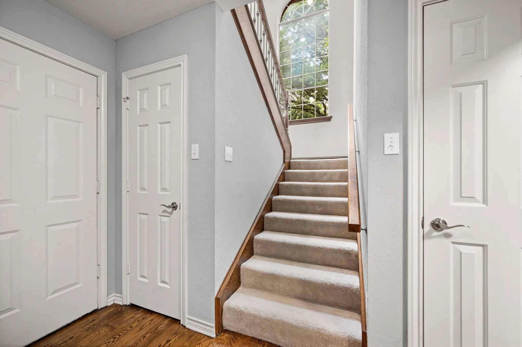 Carpeted staircase with wood handrail, featuring an arched window and paneled interior doors
