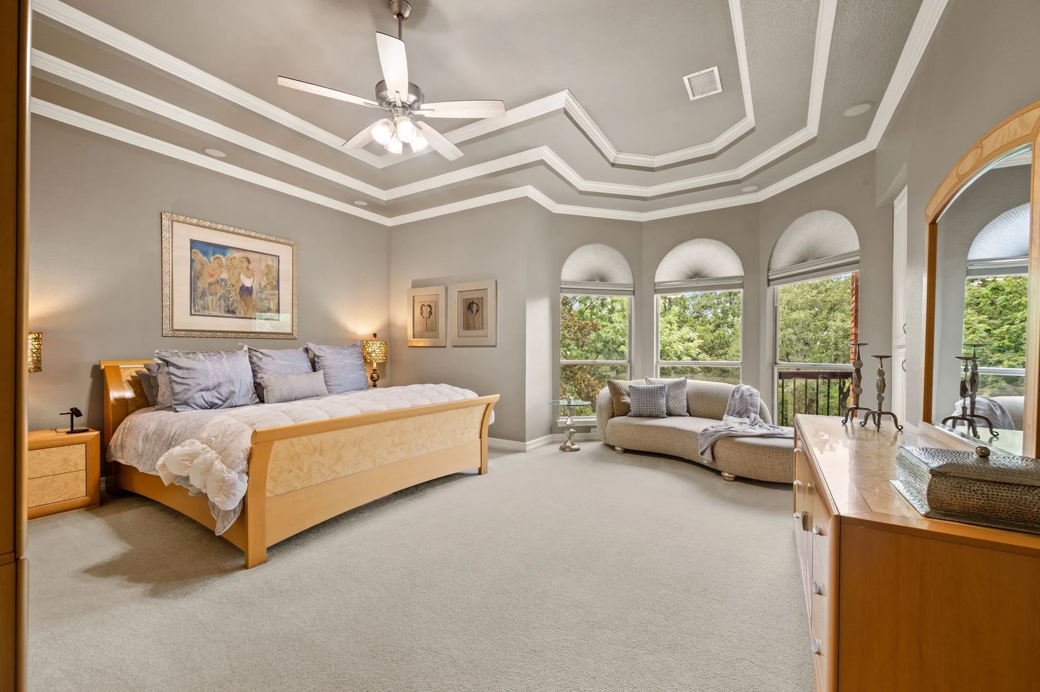 Spacious room featuring multiple arched windows, a multi-tiered tray ceiling with a ceiling fan, recessed lighting, and light-toned carpet flooring