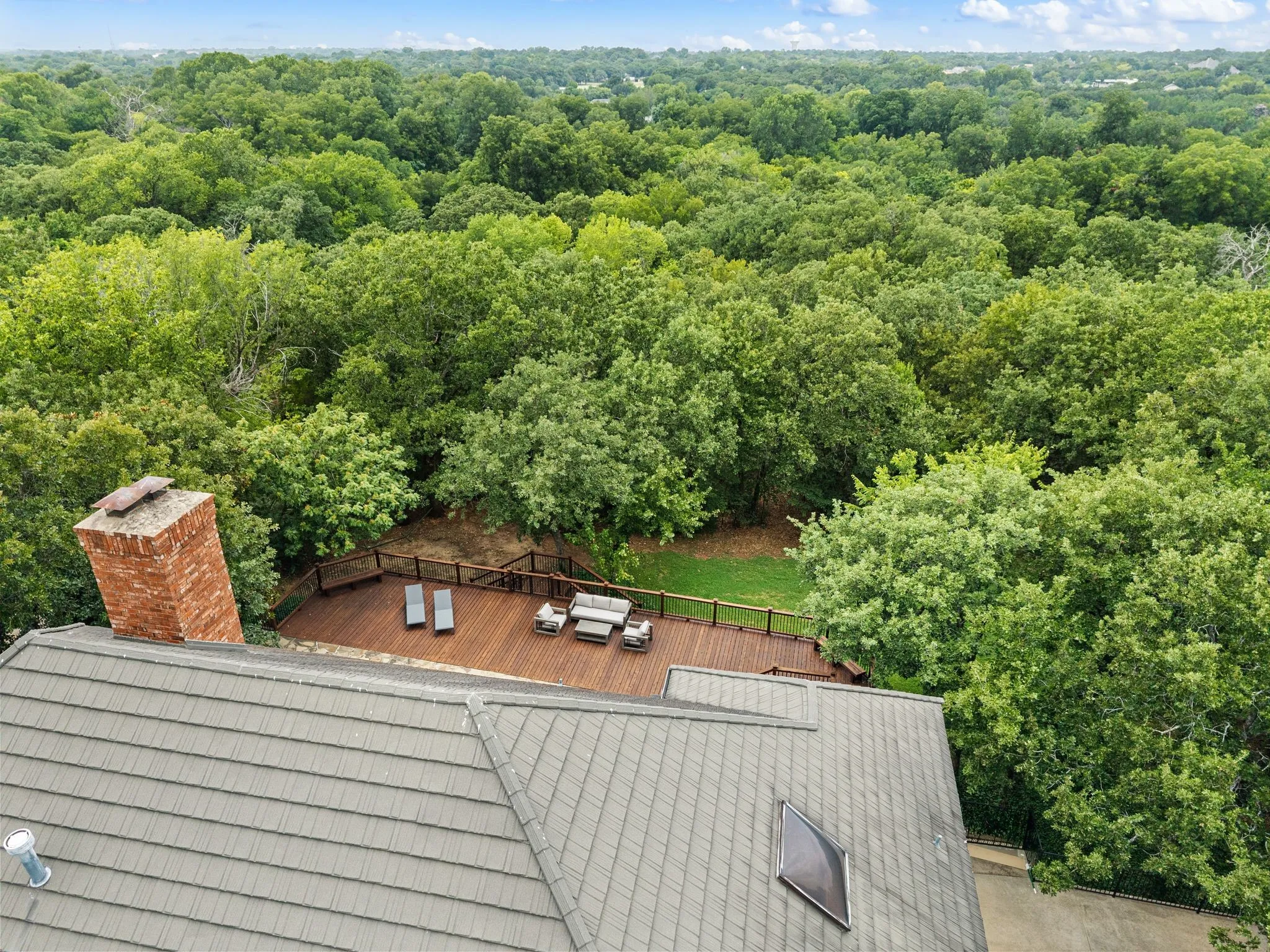 Expansive rooftop deck with wood planking and railing, surrounded by mature trees