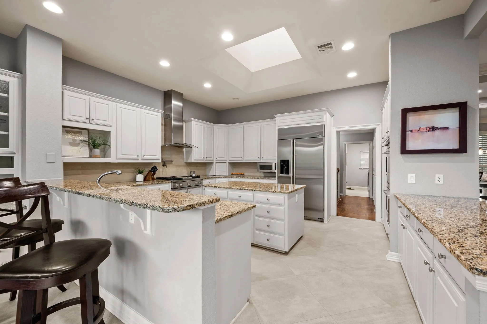Contemporary kitchen featuring white cabinetry, granite countertops, stainless steel appliances, a center island, and a skylight
