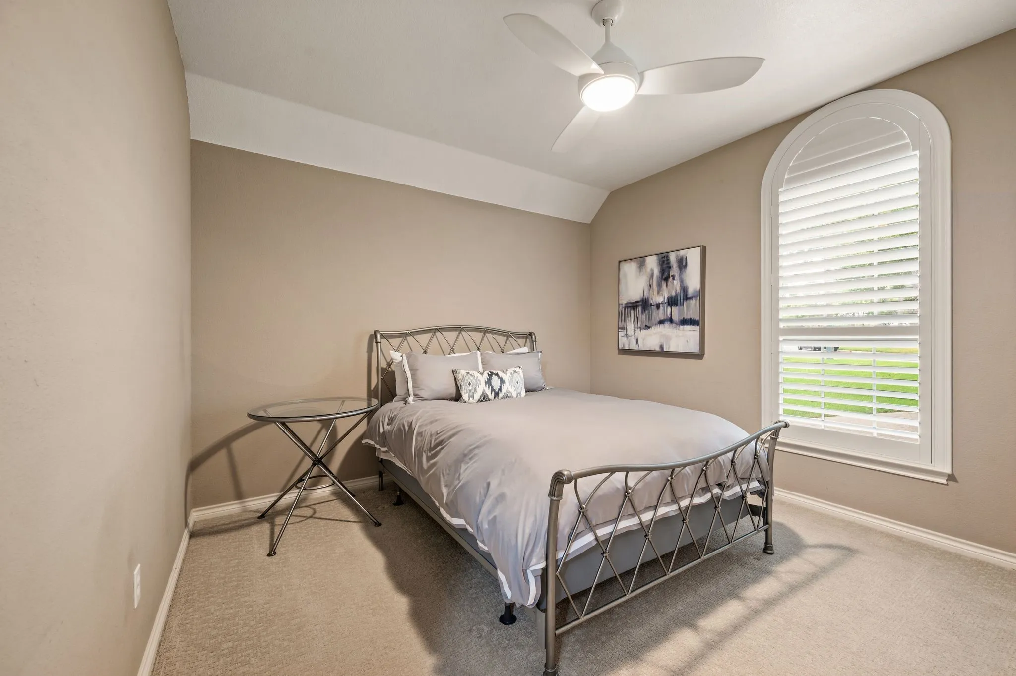 Room featuring an arched window with louvered shutters, neutral carpeting, and a ceiling fan with integrated lighting