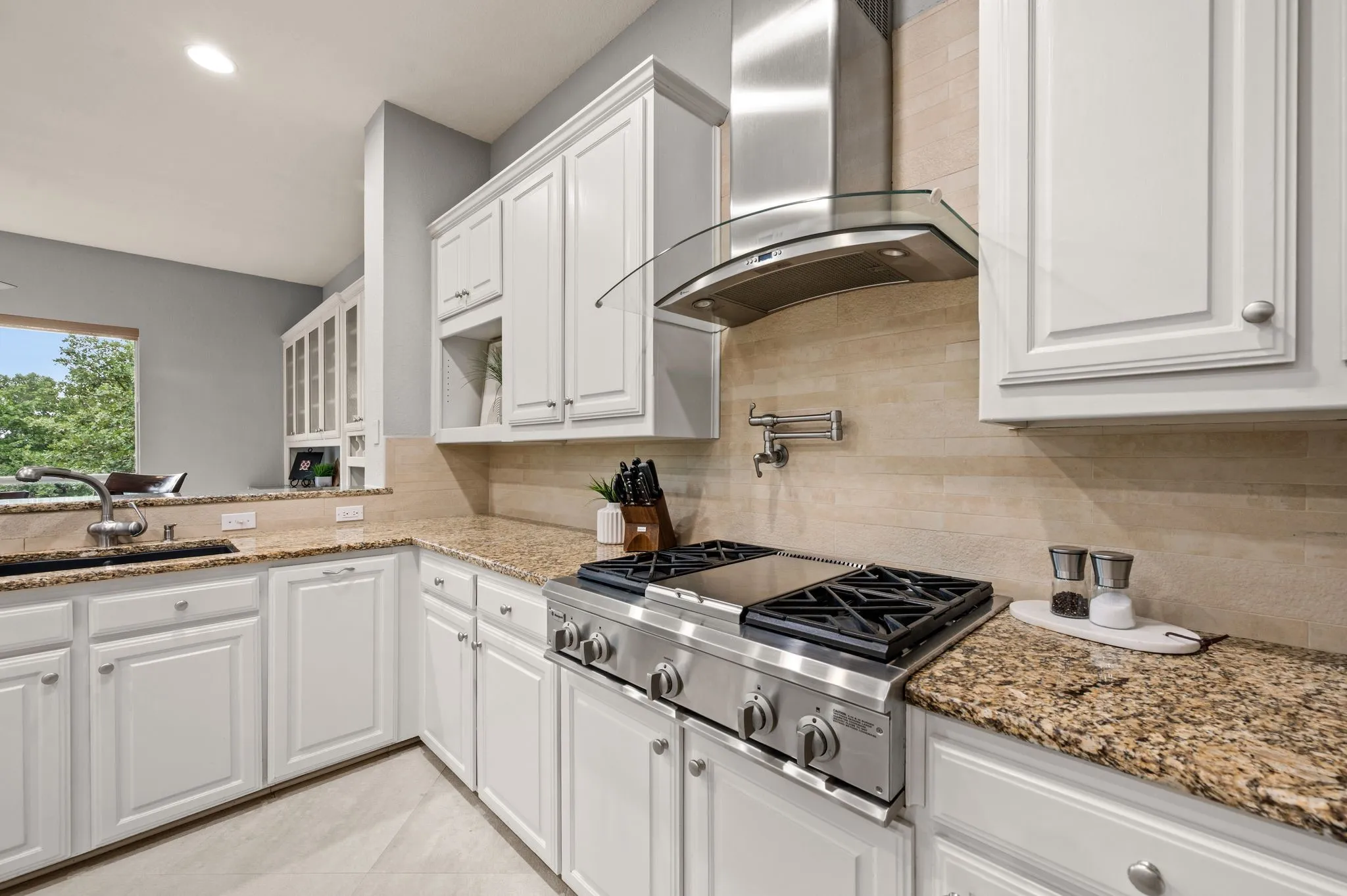 Kitchen featuring white shaker cabinetry, granite countertops, a stainless steel range with a professional-grade hood, a tile backsplash, and a pot filler faucet