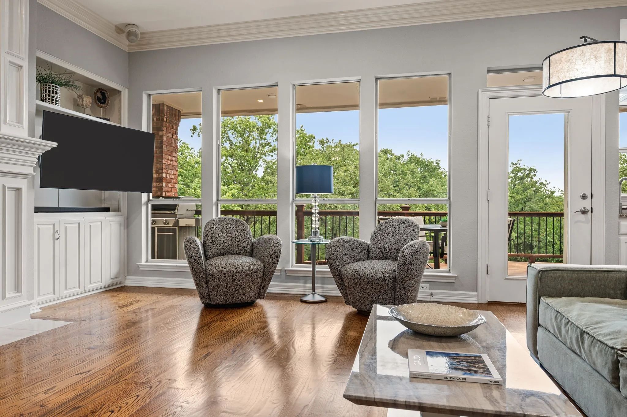 Living area featuring rich wood flooring, built-in cabinetry, multiple large windows, and a glass-paneled door opening to an exterior deck with dark railings