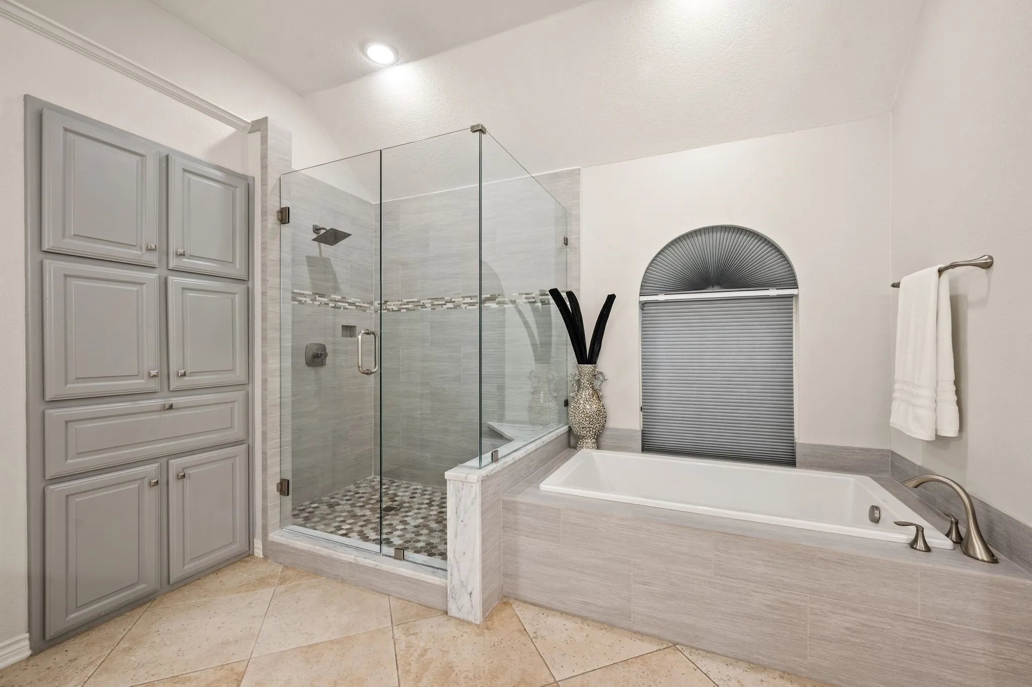 Tiled walk-in shower with glass enclosure and pebble flooring, complemented by a built-in soaking tub with brushed nickel fixtures
