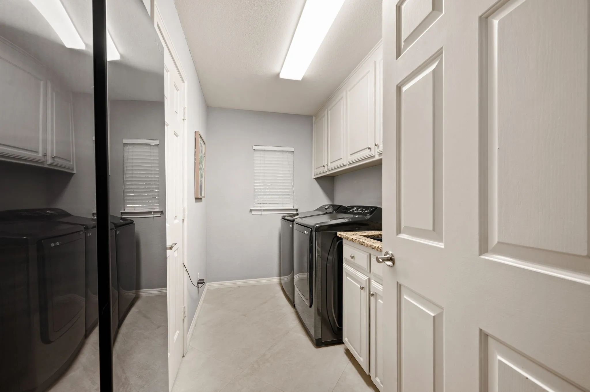 Dedicated laundry room featuring light gray walls, built-in white cabinetry, a countertop with an integrated sink, and horizontal window blinds