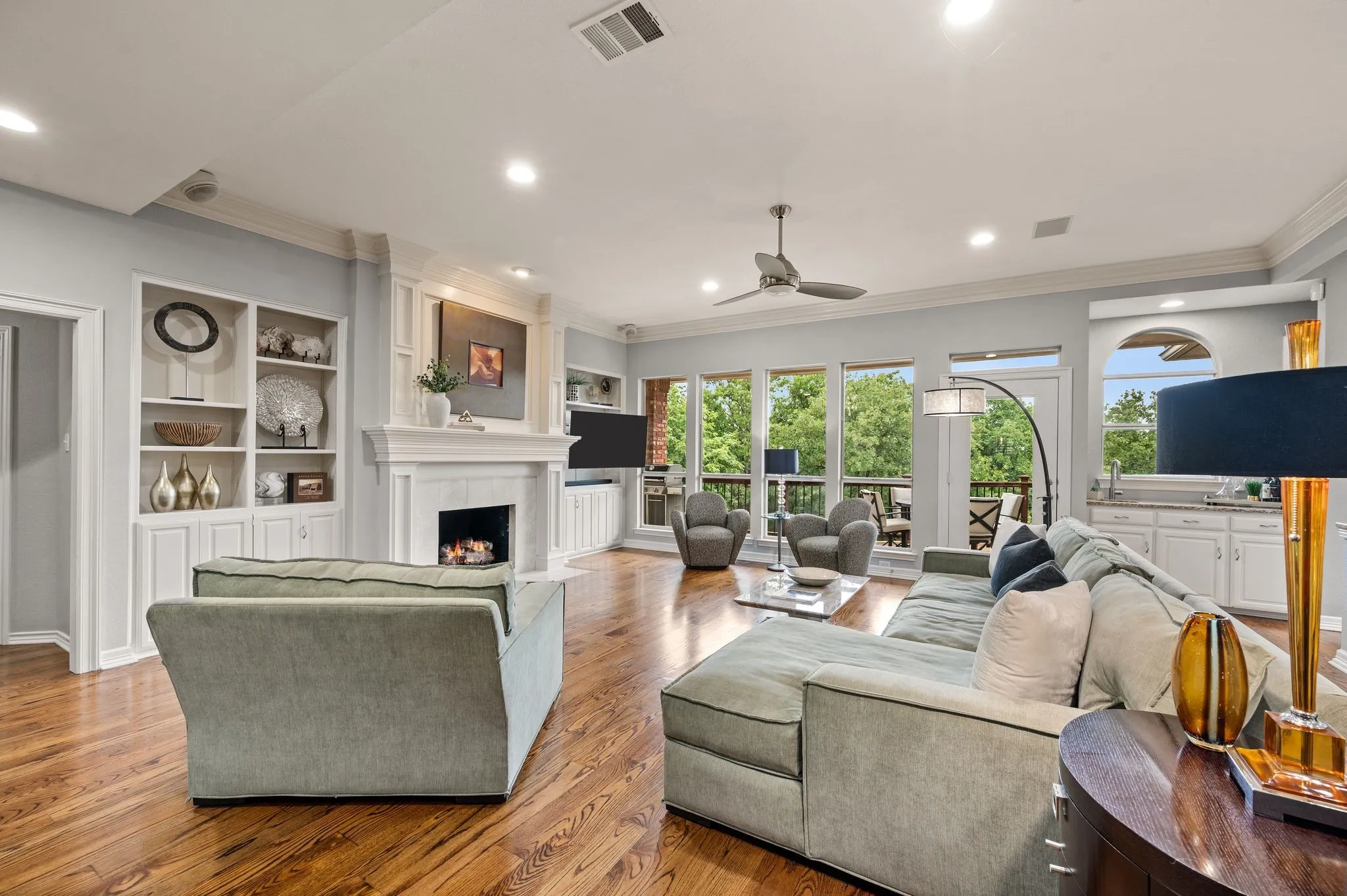 Spacious living area featuring rich wood-finish flooring, a white mantel fireplace, and built-in shelving