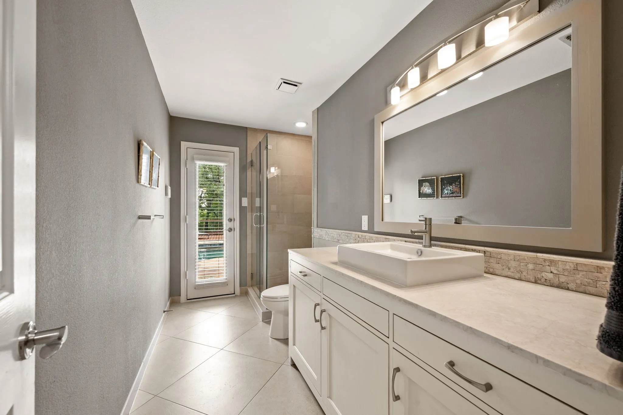 Modern bathroom featuring a single vanity with a vessel sink, a full-width mirror, and a glass-enclosed shower