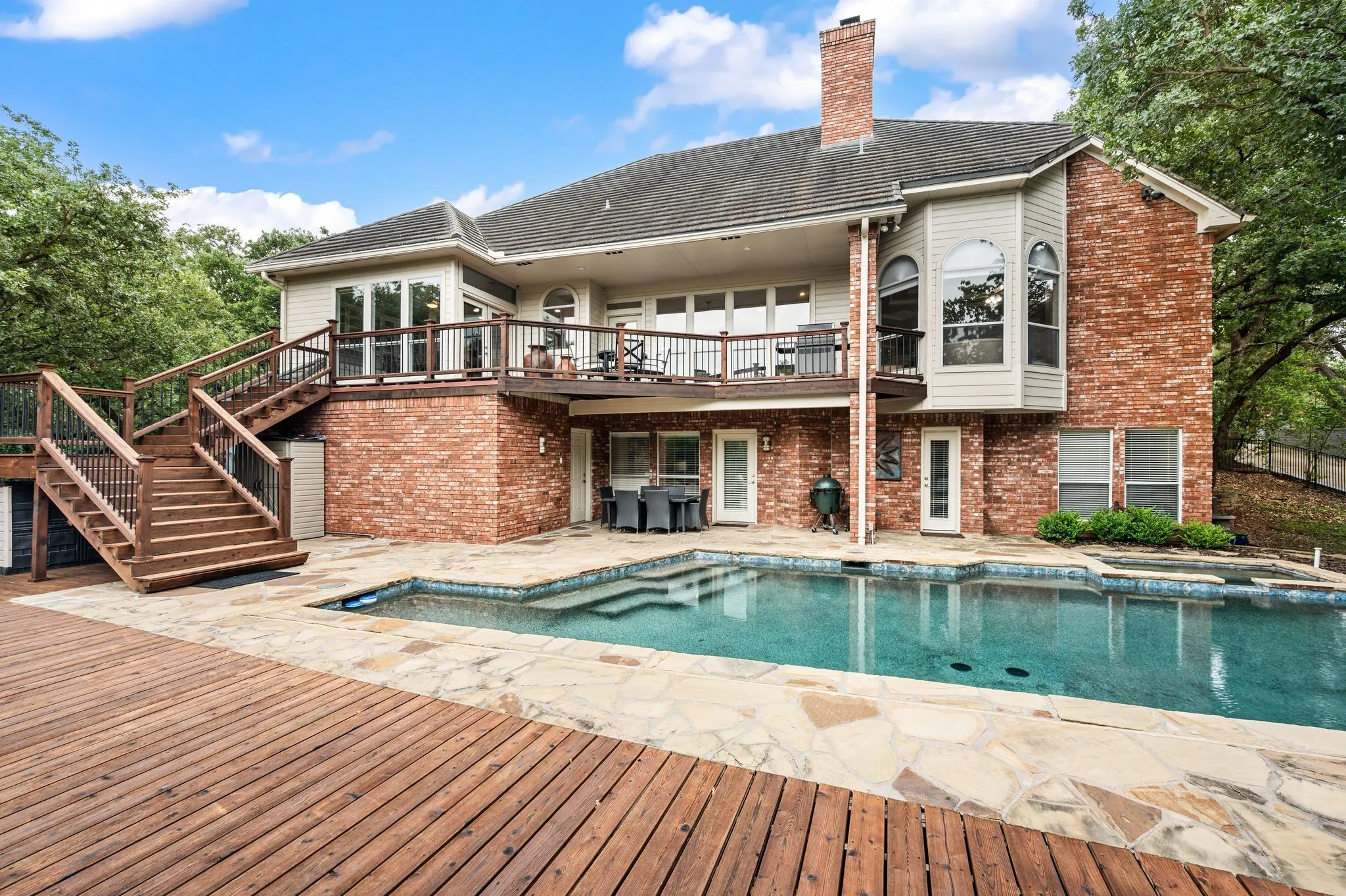 Rear exterior featuring a multi-level wood deck, an inground swimming pool with integrated spa, and a flagstone patio