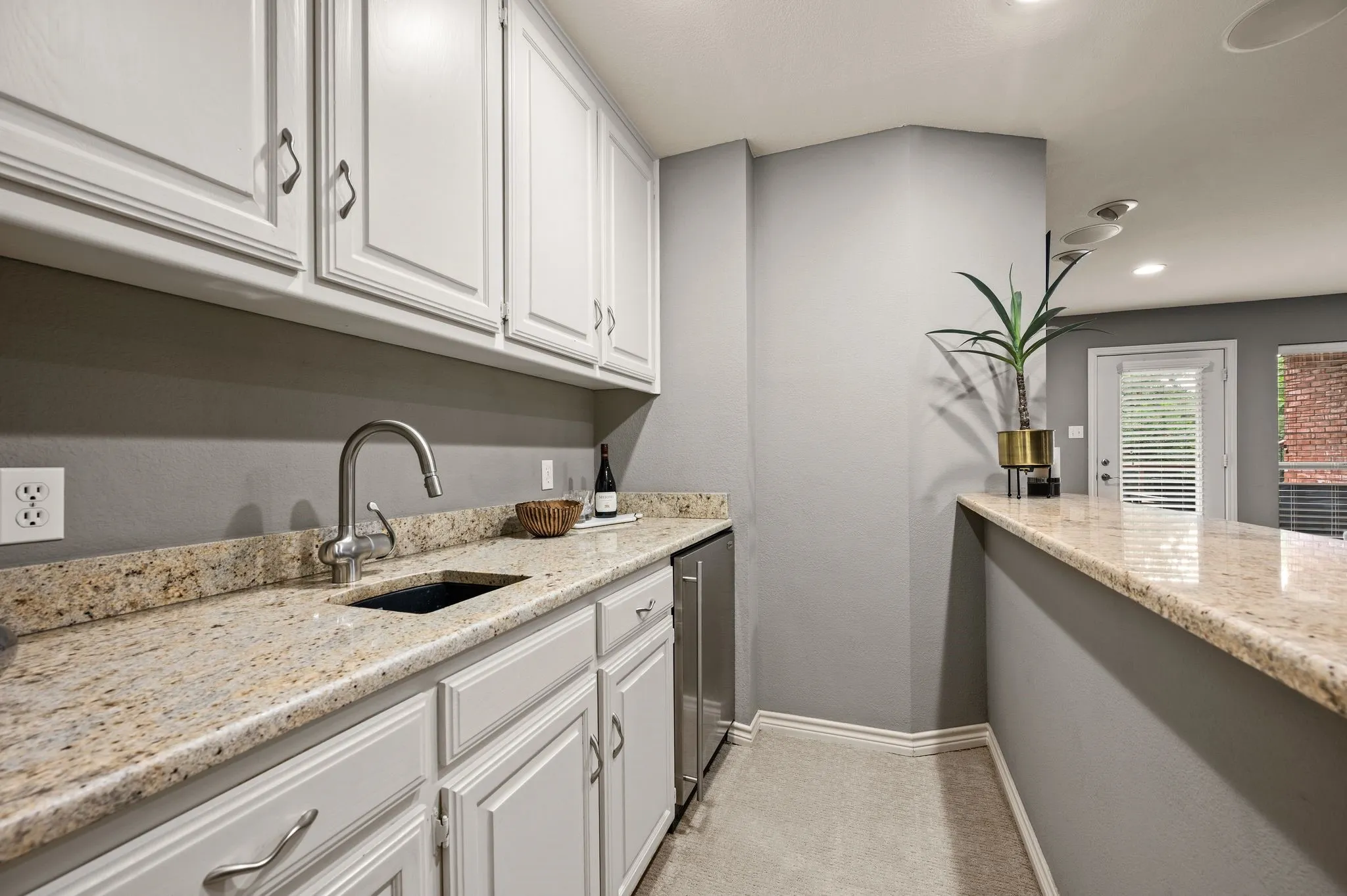 Kitchenette featuring light-toned cabinetry, a stainless steel sink with a gooseneck faucet, light-toned stone countertops, and a built-in beverage refrigerator