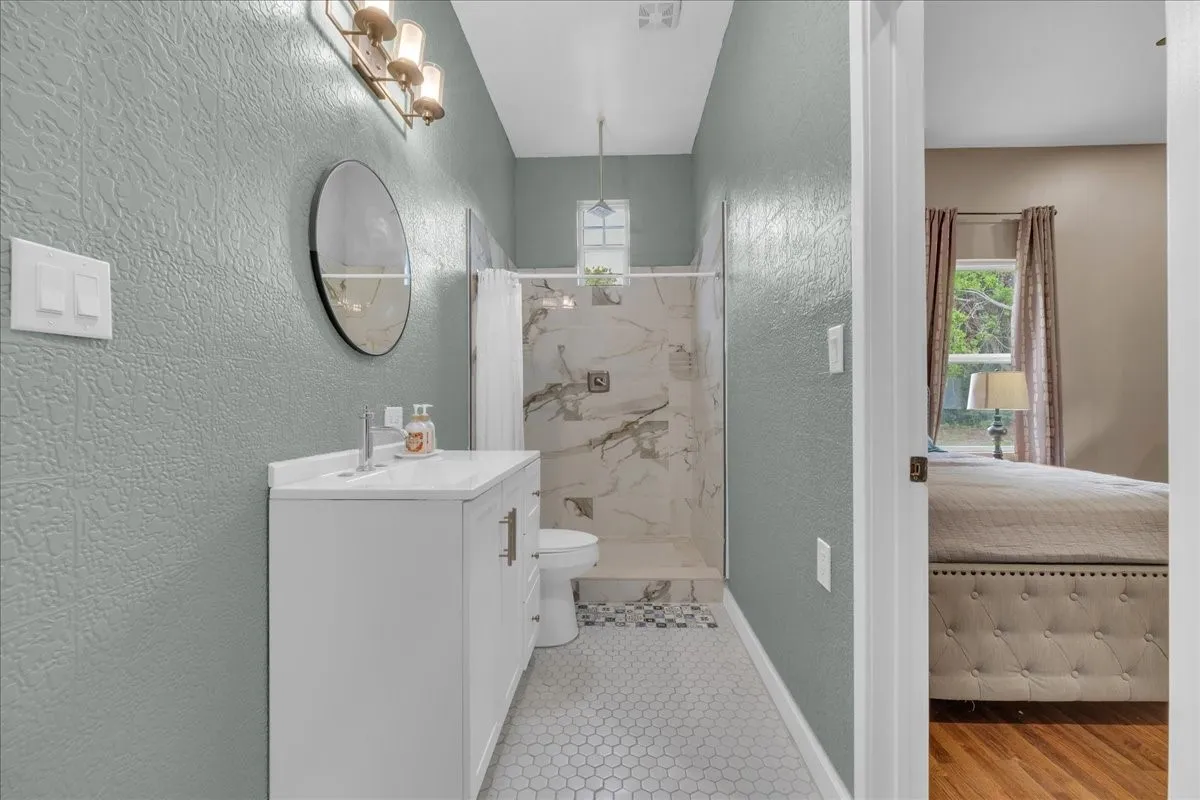 Bathroom featuring a white vanity with a rectangular sink, a shower with a glass enclosure, white and gray patterned shower tile, and hexagonal floor tiles