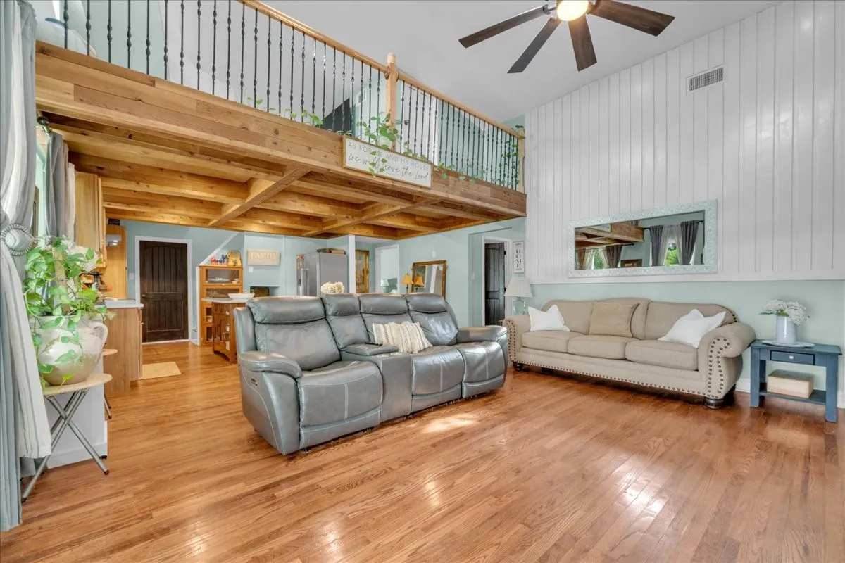 Spacious living area featuring high ceilings, wood-finish flooring, and a second-story loft with wrought iron railing