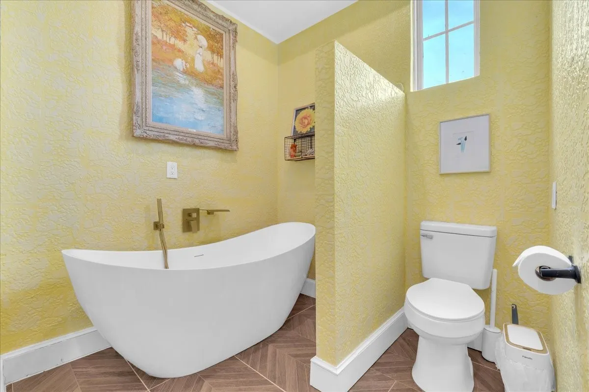 Freestanding soaking tub with a wall-mounted faucet, complemented by textured yellow walls and wood-finish herringbone flooring