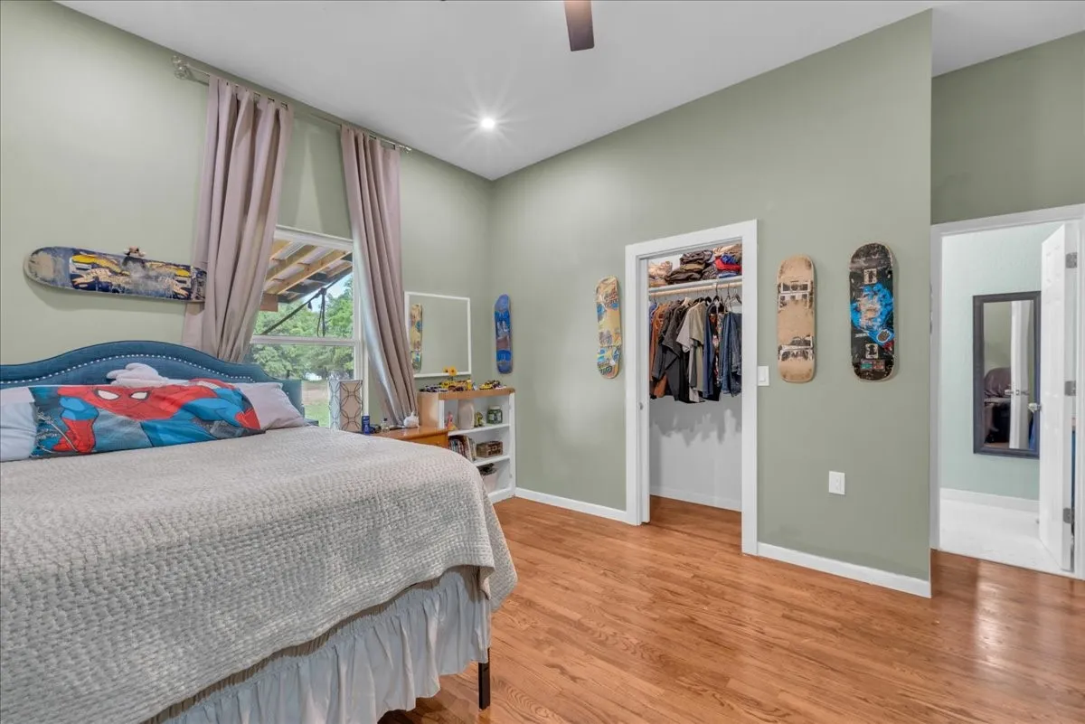 Bedroom with light green walls, wood-finish flooring, a ceiling fan, and a window with light-colored drapes