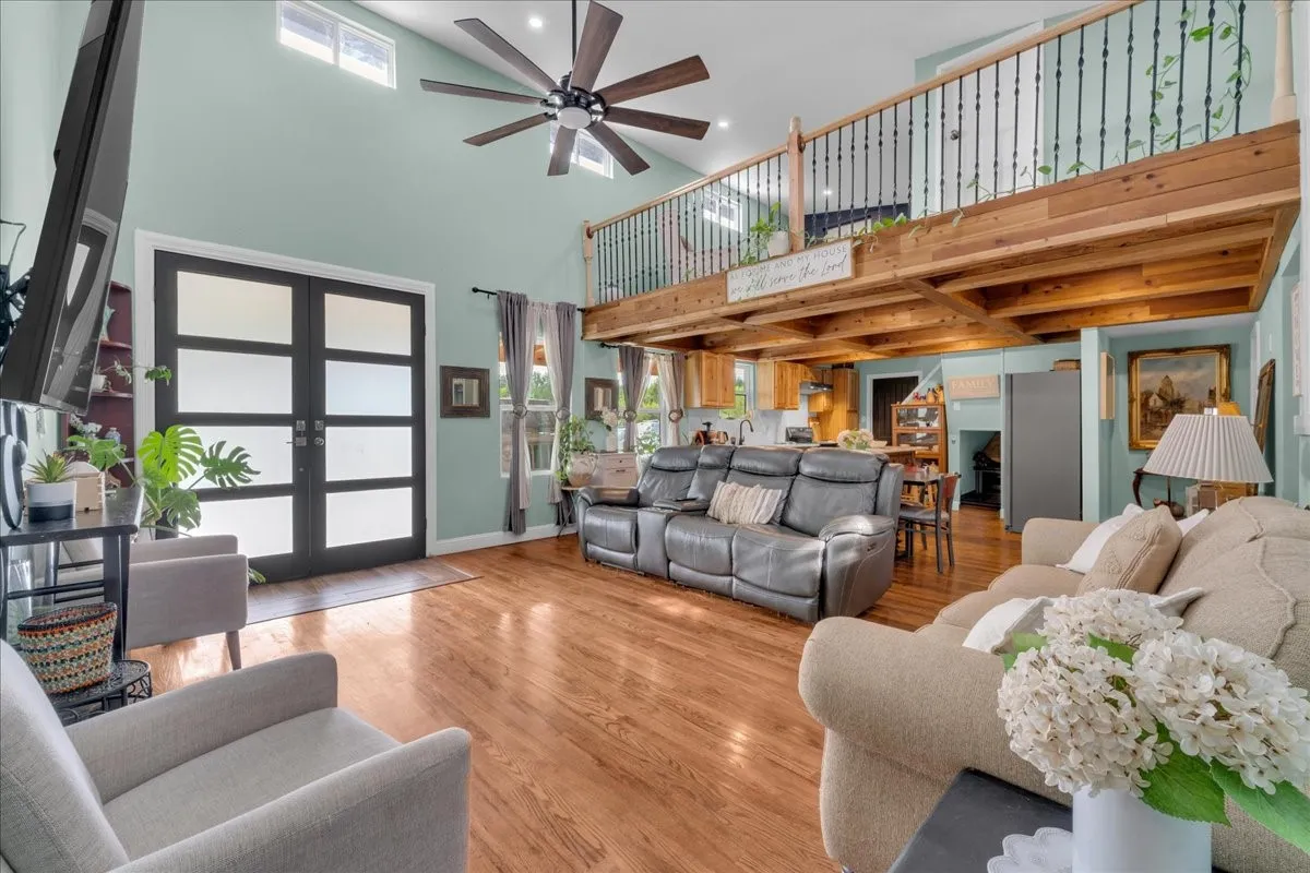 Spacious living area featuring high vaulted ceilings, light wood-finish flooring, and a prominent loft with a dark metal railing