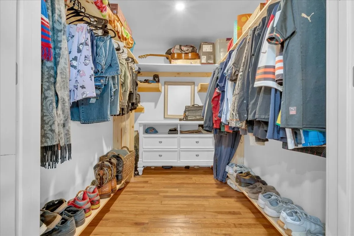 Custom closet system featuring wood-finish flooring, white walls, and recessed lighting