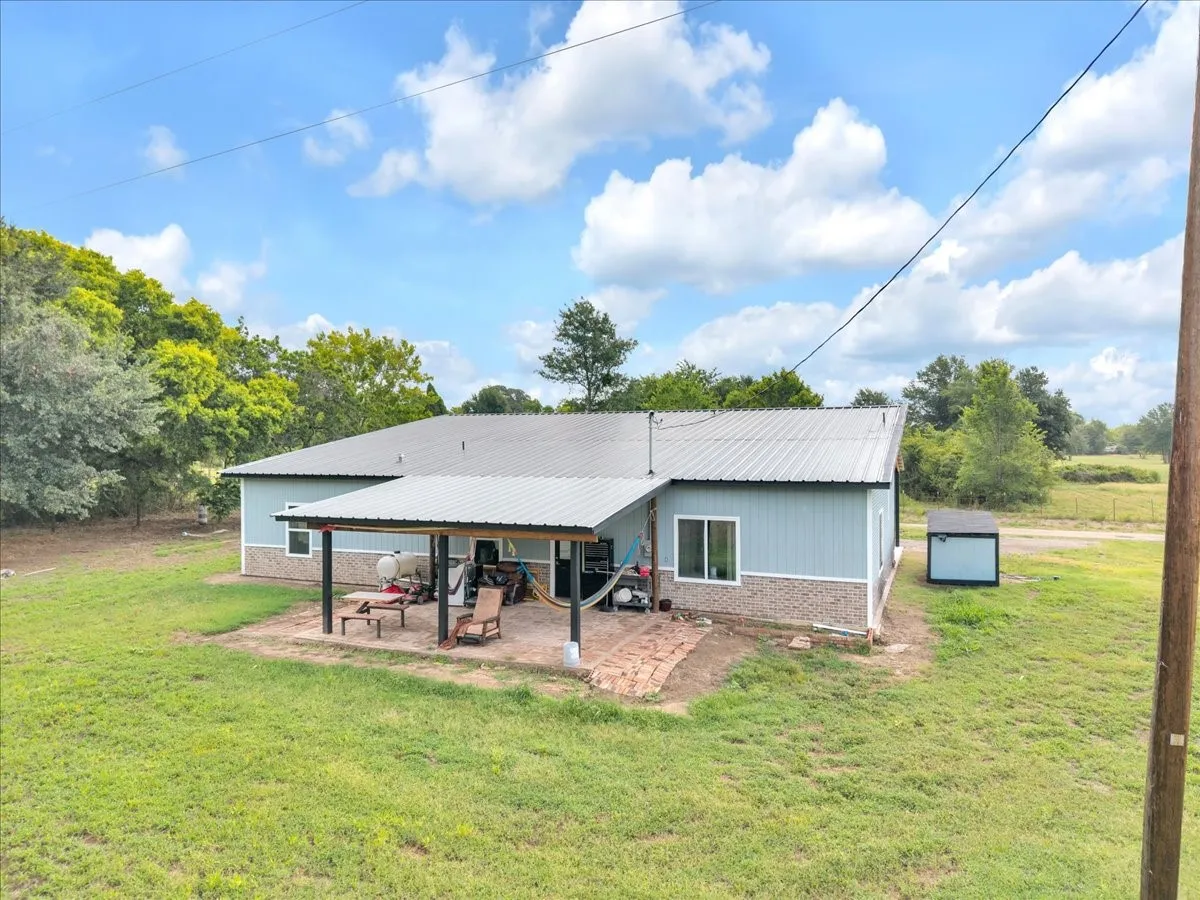 Rear exterior featuring a covered patio with brick paver flooring, light blue siding, and a metal roof