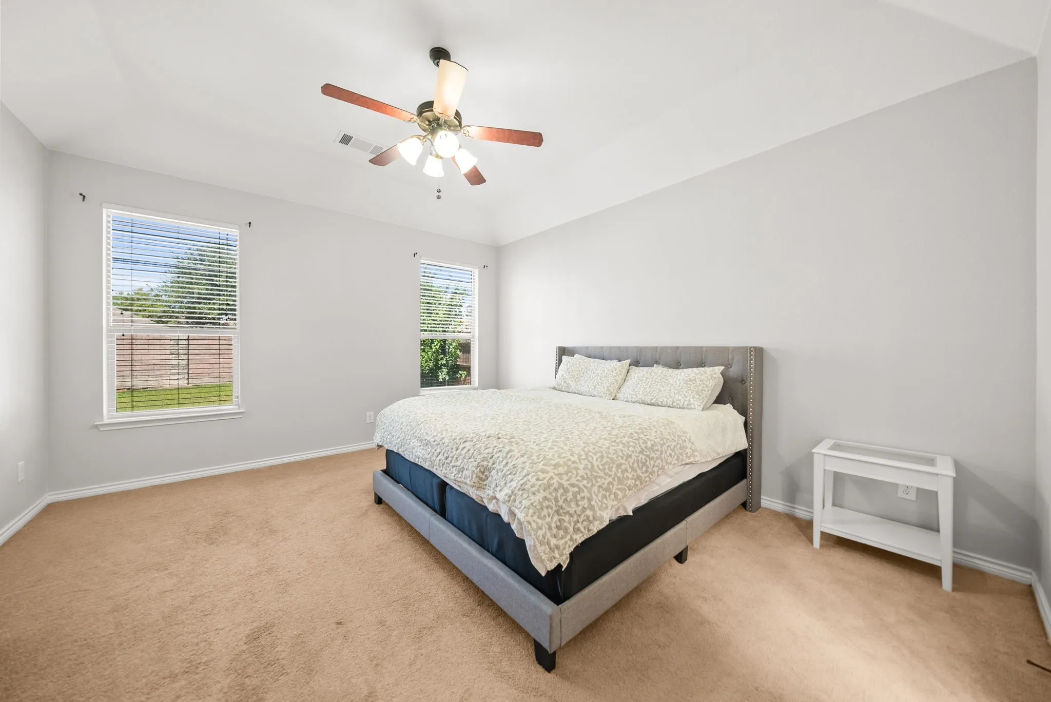 Carpeted room featuring a vaulted ceiling with a ceiling fan, two windows with blinds, and light-colored walls