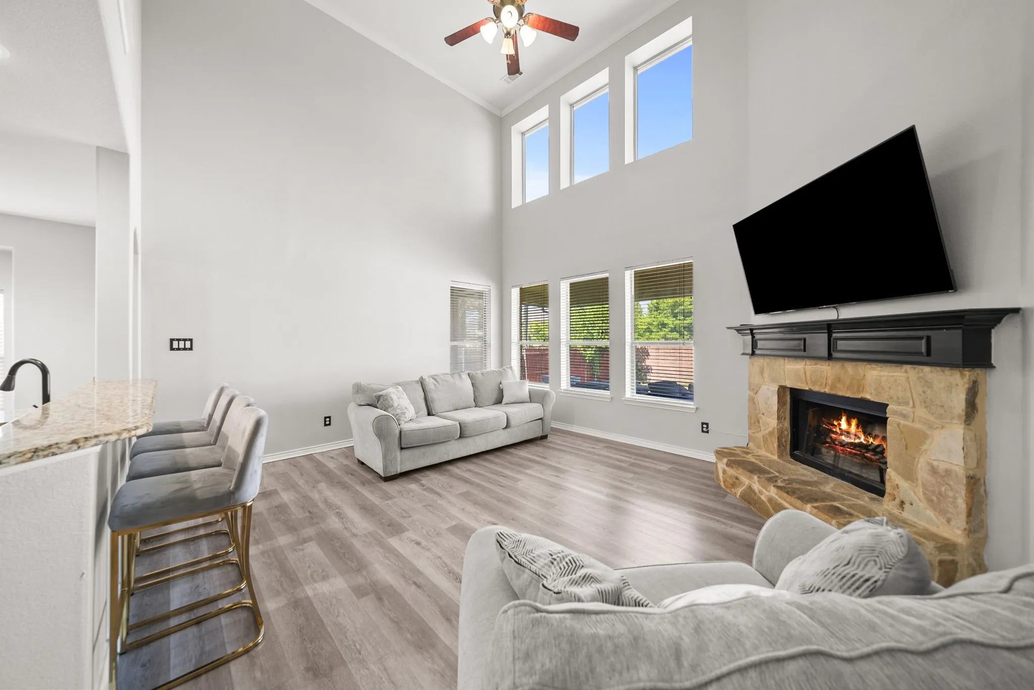 Living area featuring a stone-clad fireplace with a dark wood mantel, high ceilings, wood-finish flooring, and multiple windows