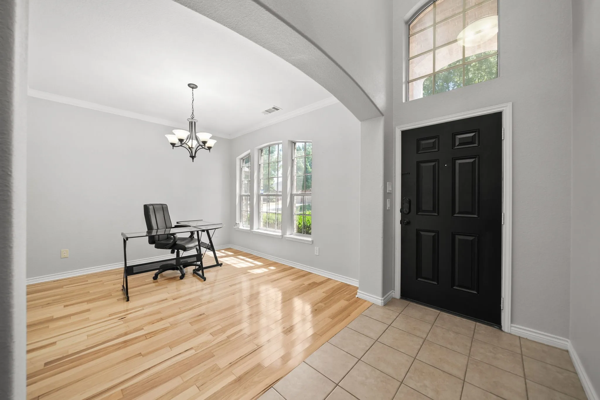 Entry area featuring a paneled black door with arched transom window, tiled flooring, and an arched doorway opening to a room with wood-finish flooring, a multi-pane bay window, and a chandelier