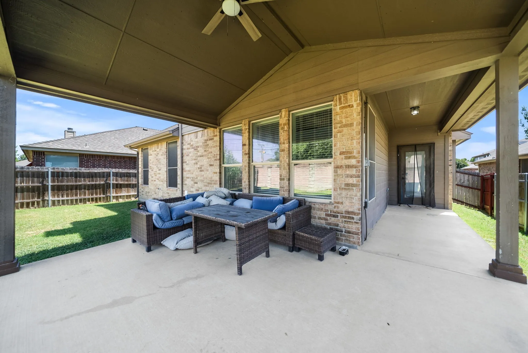 Expansive covered patio featuring a ceiling fan, concrete flooring, brick exterior, and multiple windows with blinds