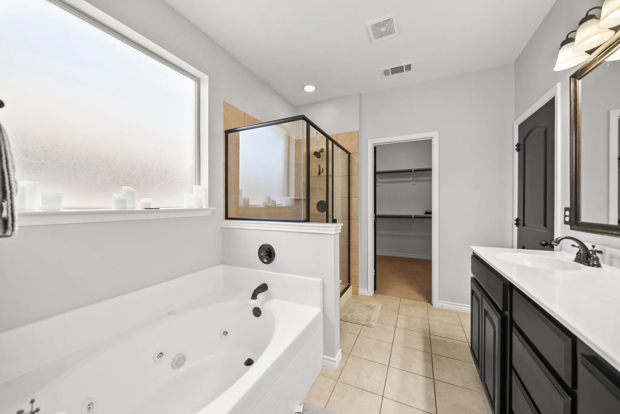Bathroom featuring a built-in jetted tub, a separate glass-enclosed shower with tile surround, a single vanity with a white countertop, and tile flooring