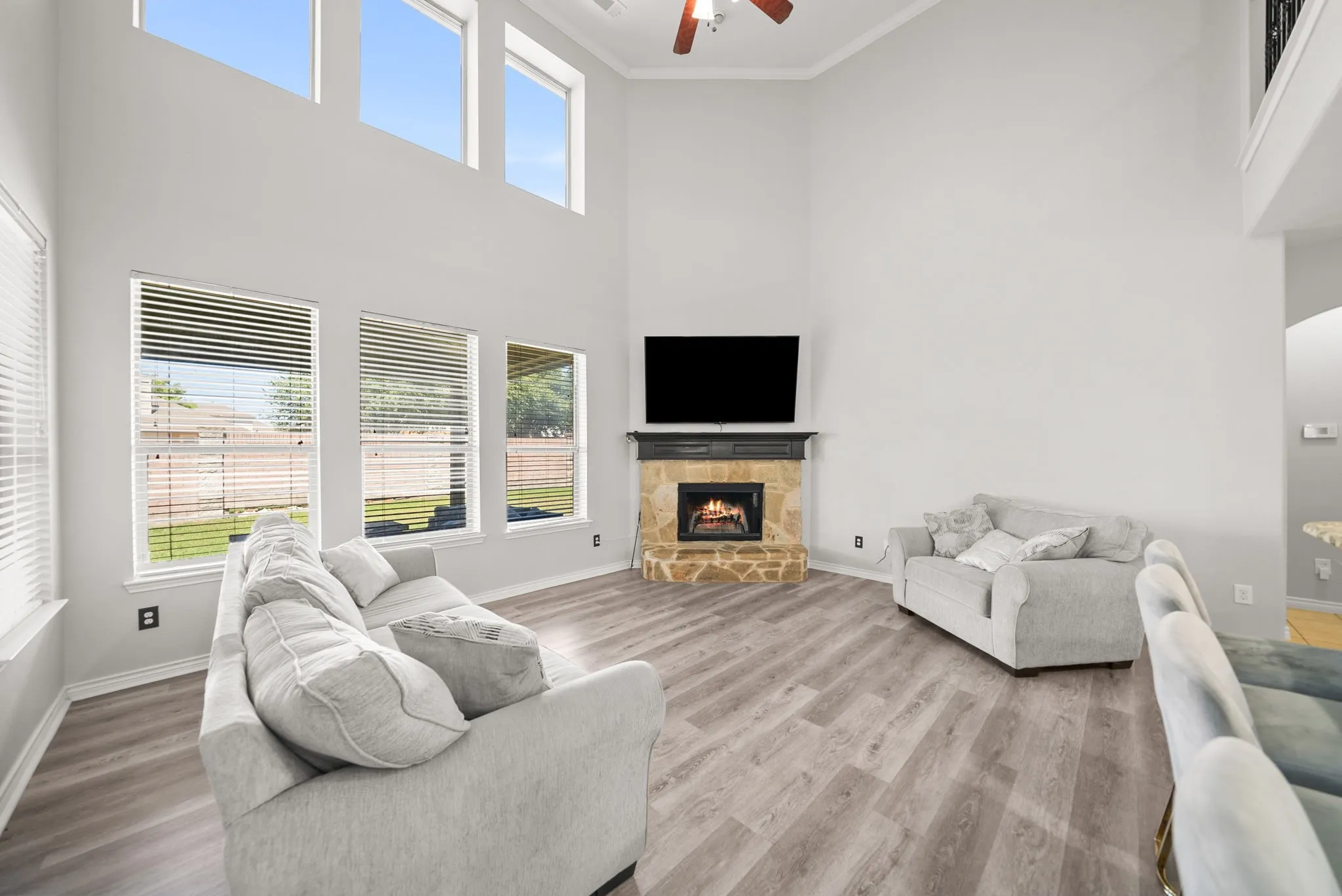 Vaulted ceiling living area featuring a stone-surround fireplace, wood-finish flooring, and multiple windows with blinds