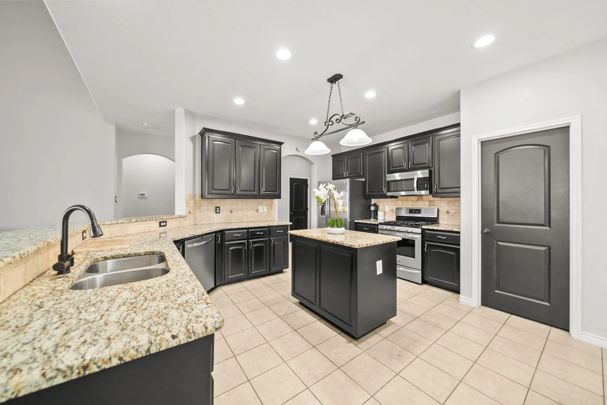 Kitchen featuring dark cabinetry, light granite countertops, stainless steel appliances, a center island, and tile flooring