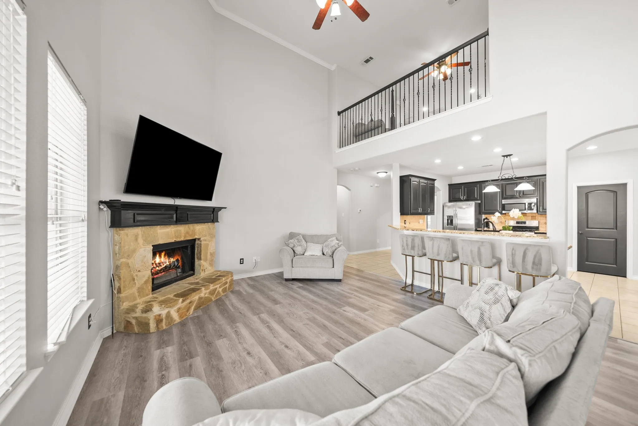 Spacious living area featuring a stone-clad fireplace, soaring ceiling, wood-finish flooring, and a second-story balcony overlooking the space