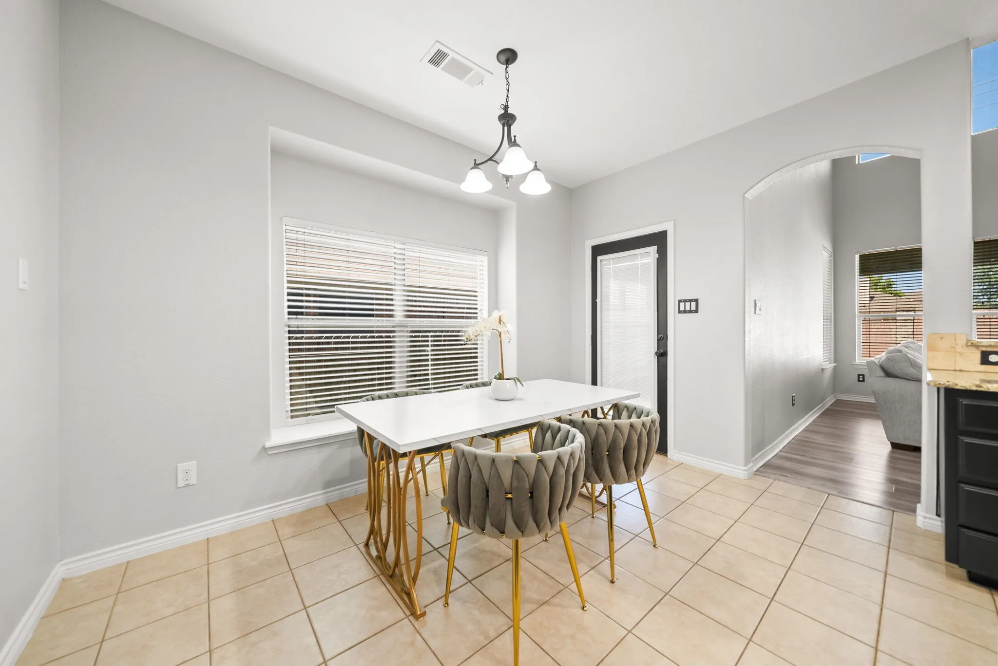 Dining space featuring tile flooring, a window with blinds, a black door, and an arched entryway to a room with wood-finish flooring