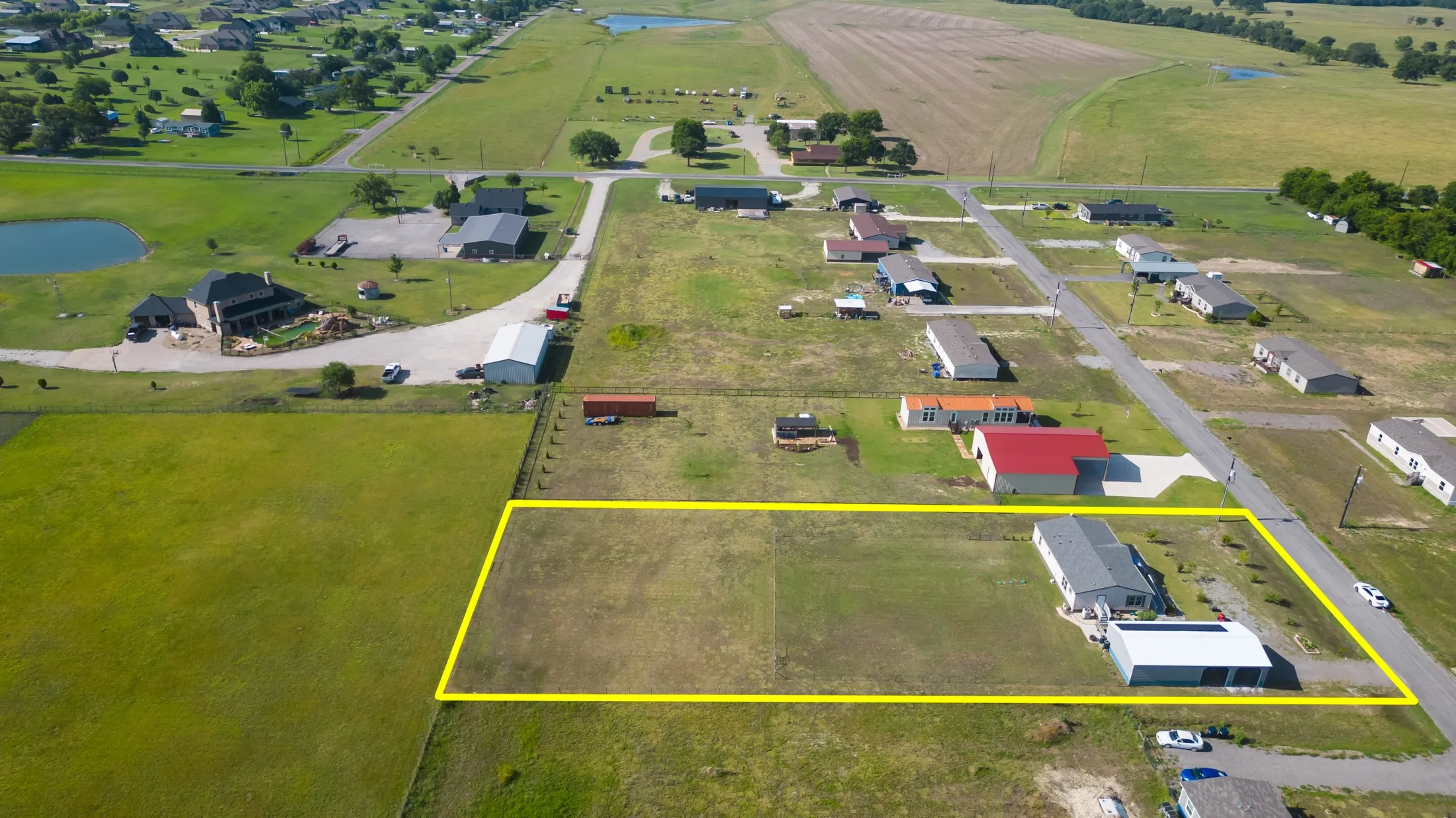 Expansive parcel featuring an existing structure and a large open field, bordered by a paved road