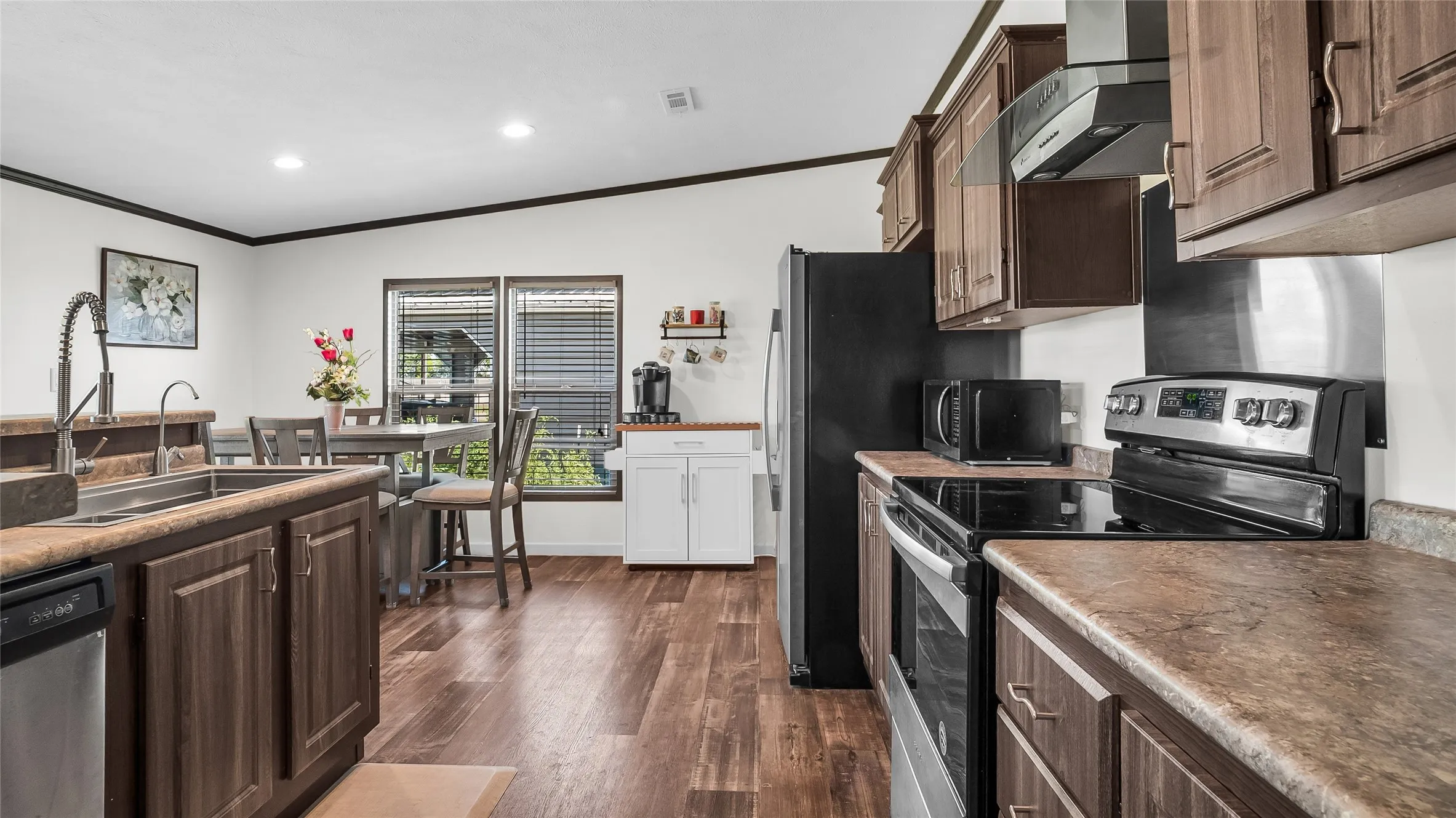 Open-concept kitchen featuring laminate flooring, dark wood cabinetry, and stainless steel appliances including a range, dishwasher, and refrigerator