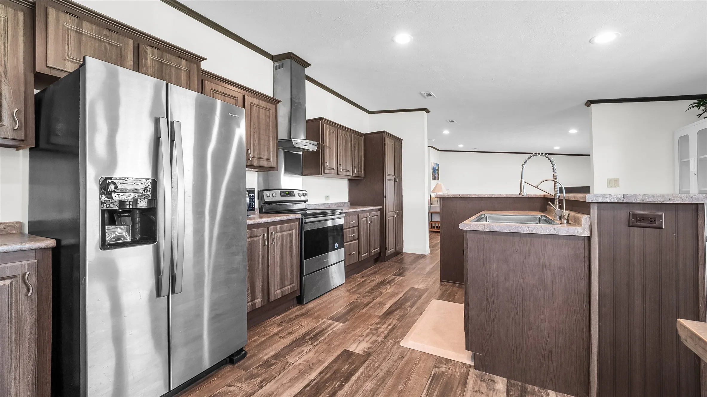 Spacious kitchen featuring laminate flooring, dark wood cabinetry, a stainless steel refrigerator, and a stainless steel oven with a range hood