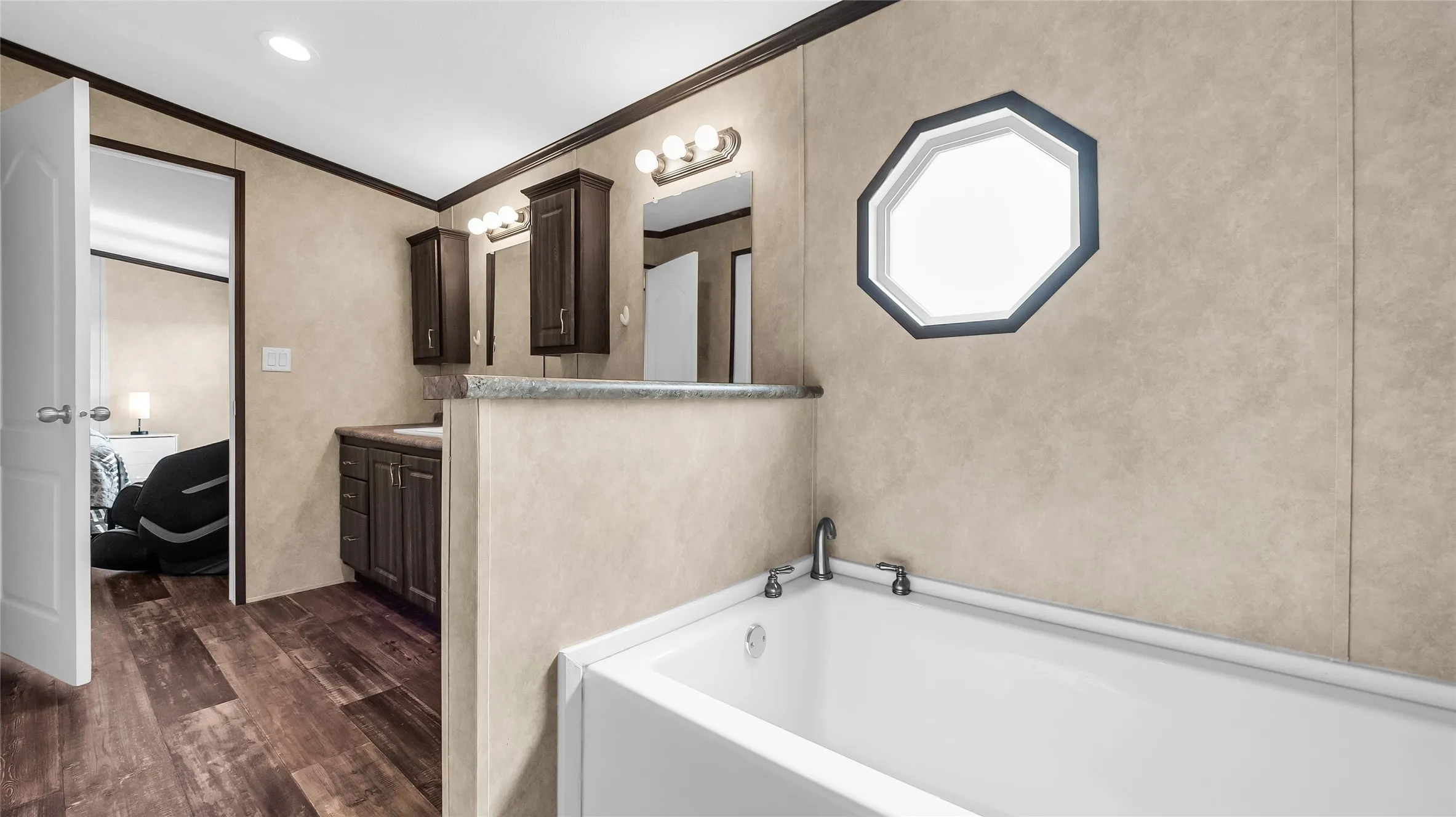 Primary Bathroom featuring a soaking tub with mounted fixtures, an octagonal window, and laminate flooring