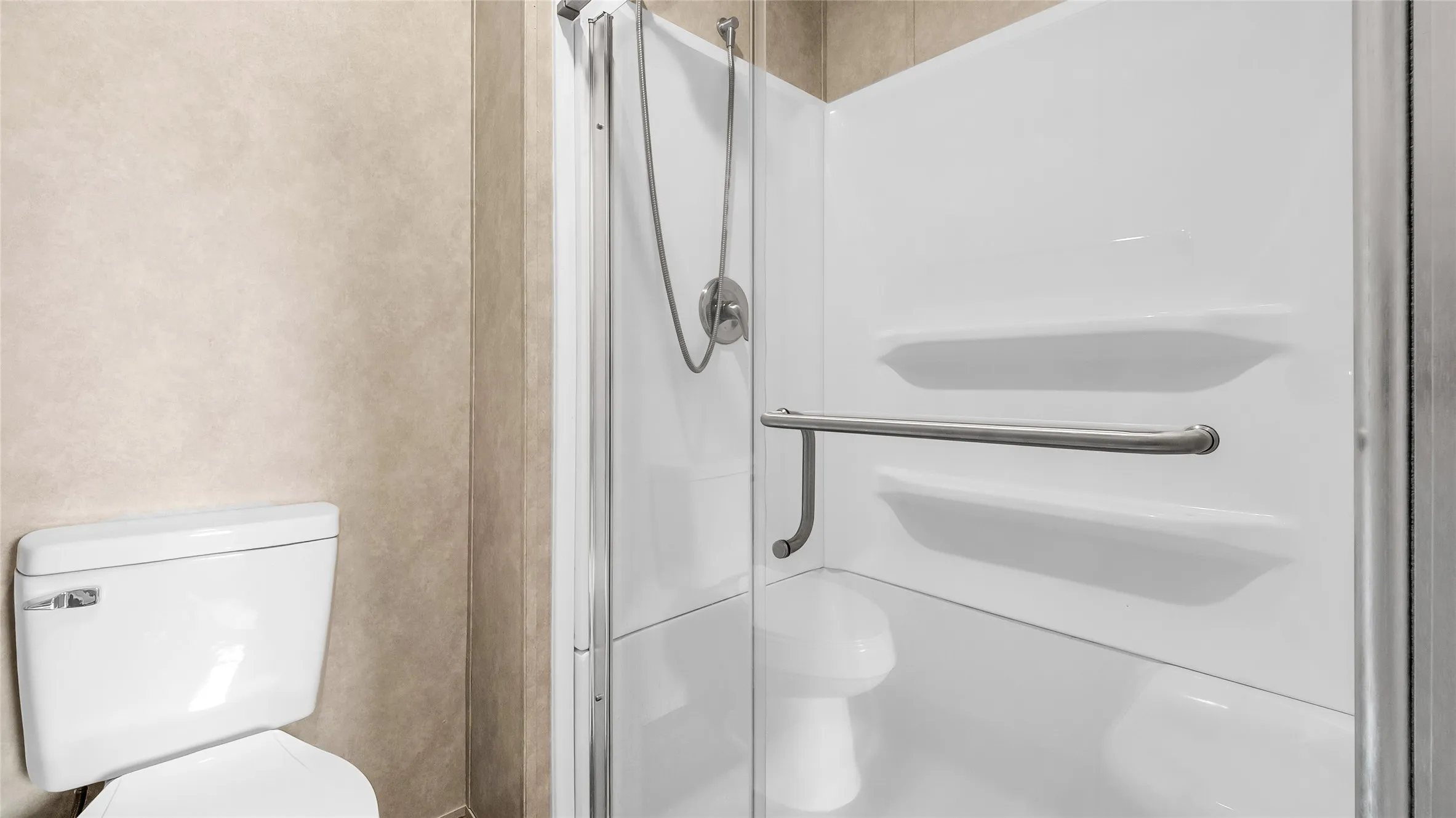 Enclosed shower stall with clear glass door, integrated shelving, and a chrome grab bar