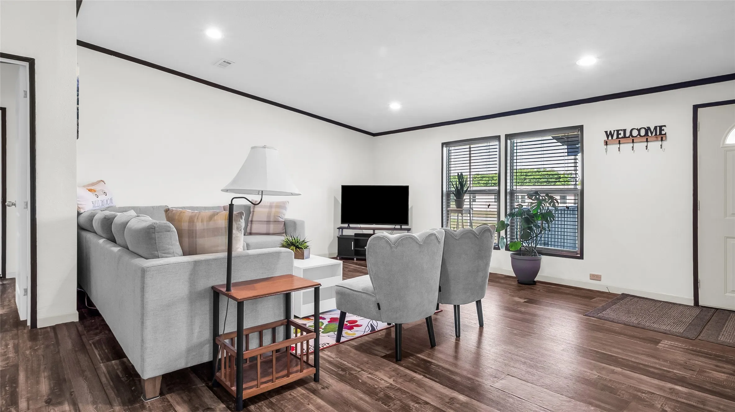 Open-concept living area featuring rich laminate flooring, white walls with dark trim, recessed lighting, and multiple windows with blinds