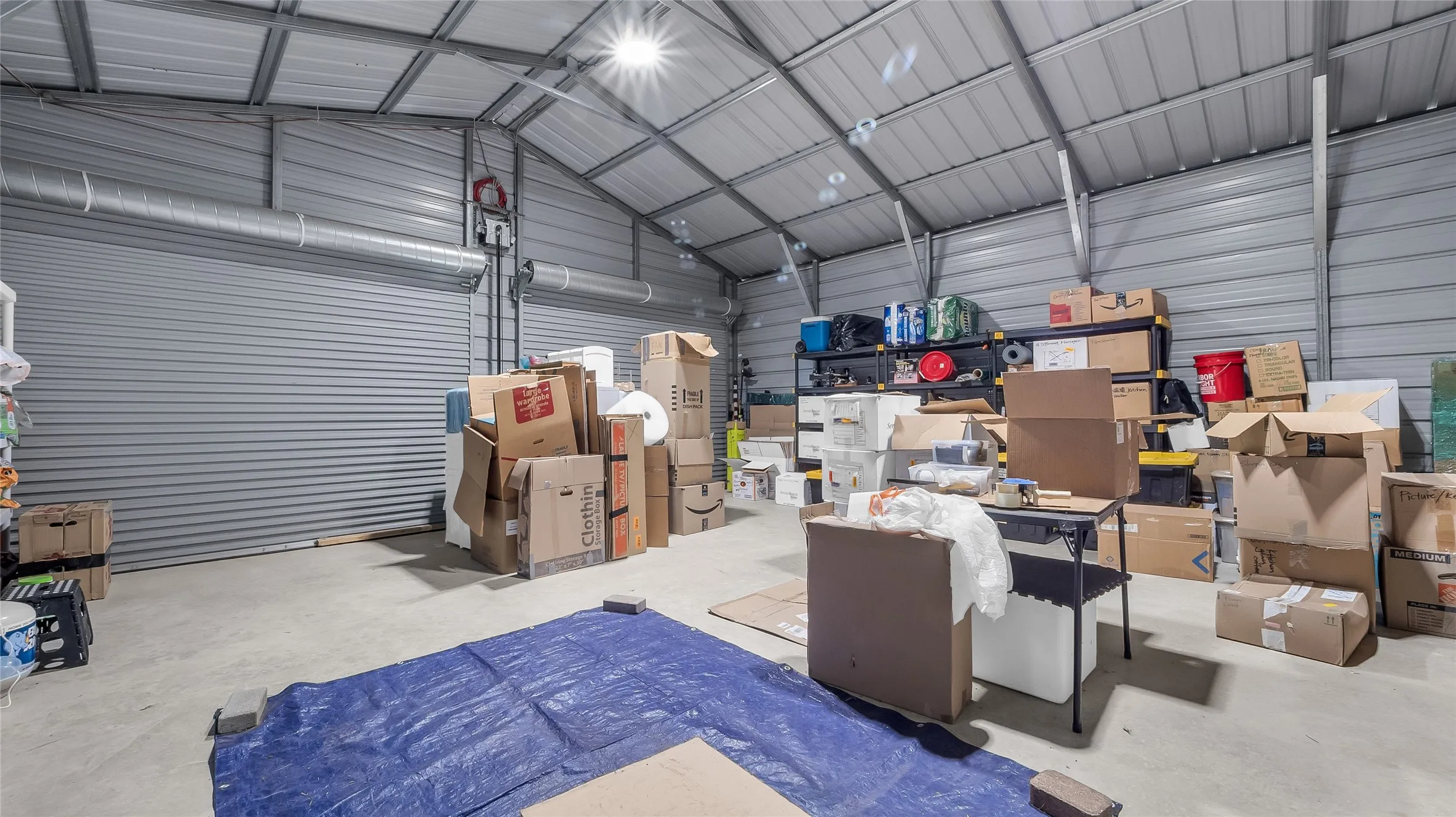 Spacious metal building with a concrete floor, high vaulted ceiling, and overhead lighting