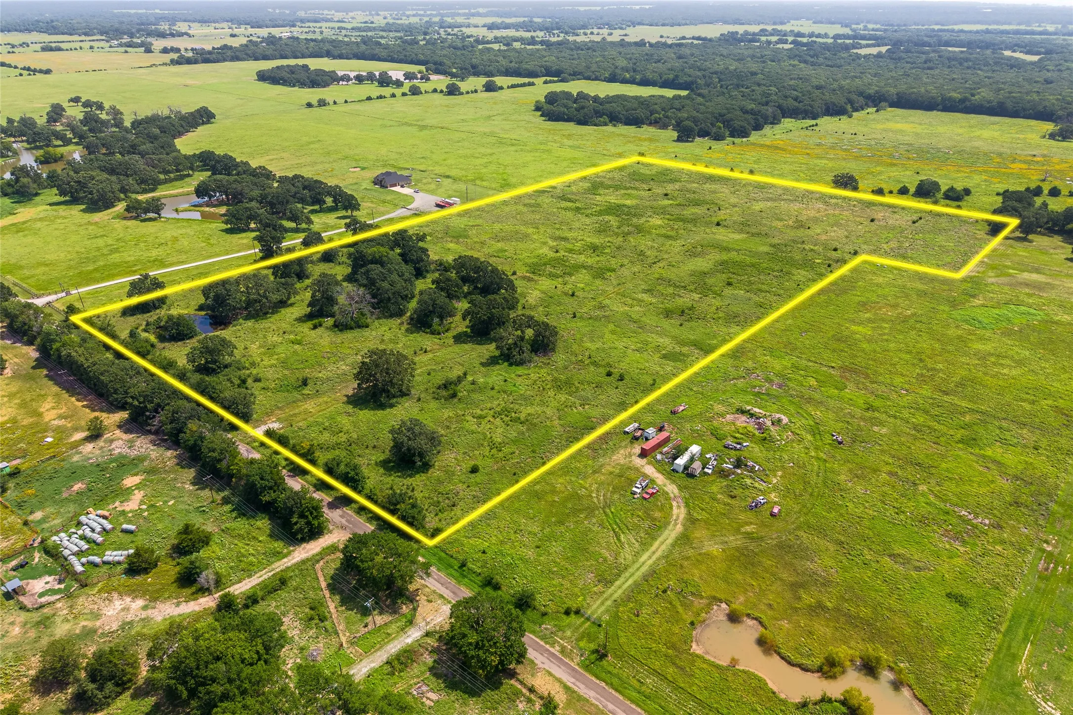 Aerial shot of 27+ acres with mature trees, pond, and open pasture looking SW