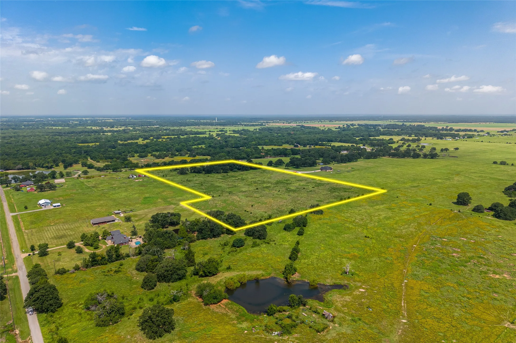 Aerial shot of 27+ acres with mature trees, pond, and open pasture looking SE